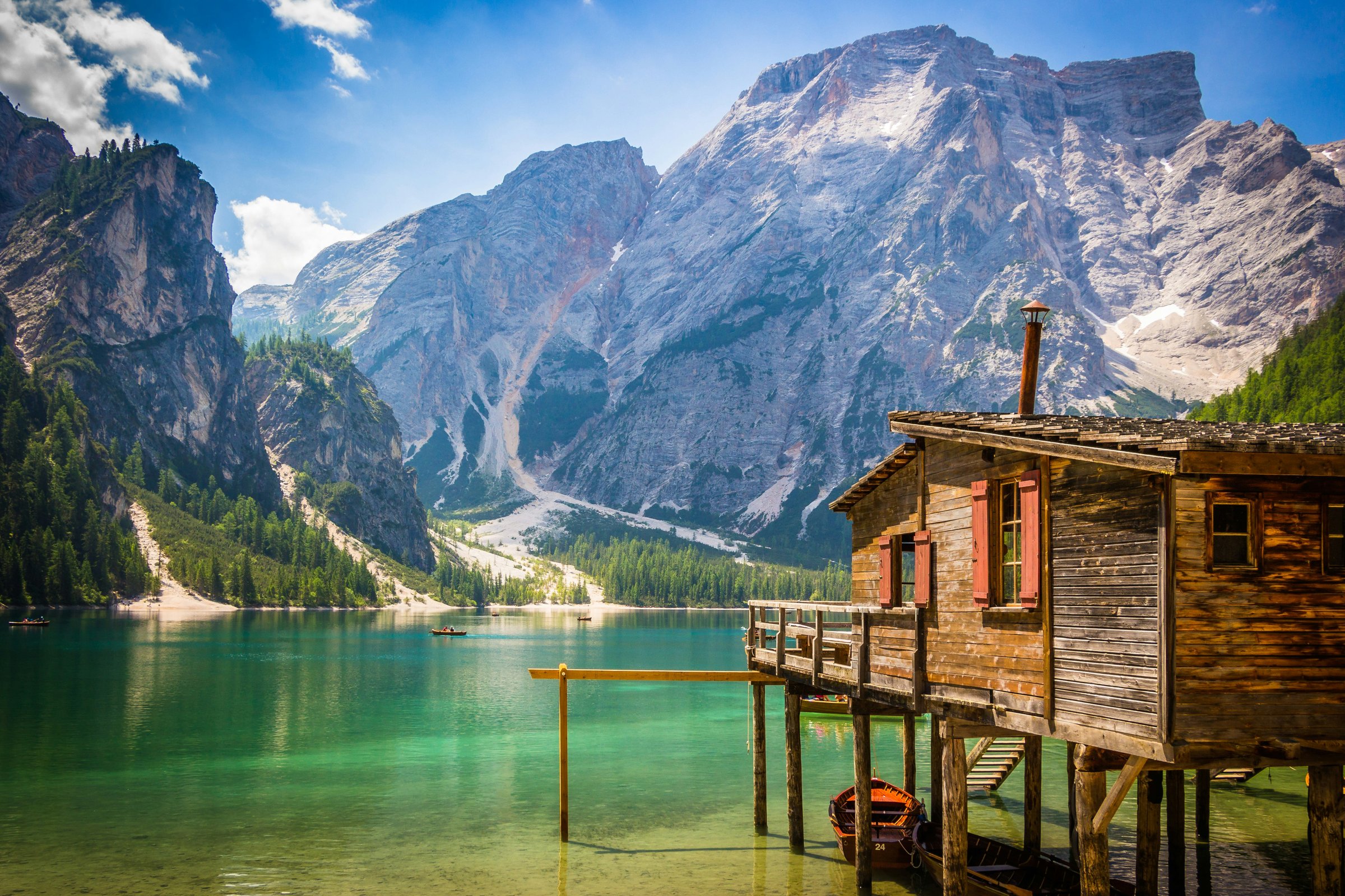 Danau Braies berwarna hijau toska dengan pondok kayu di tepi air dan Pegunungan Dolomites di belakangnya, Italia