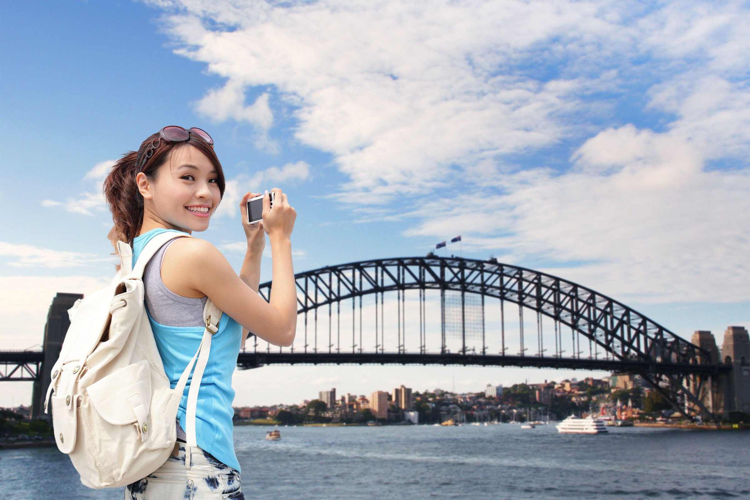Wisatawan perempuan memotret dengan latar Sydney Harbour Bridge di bawah langit biru cerah