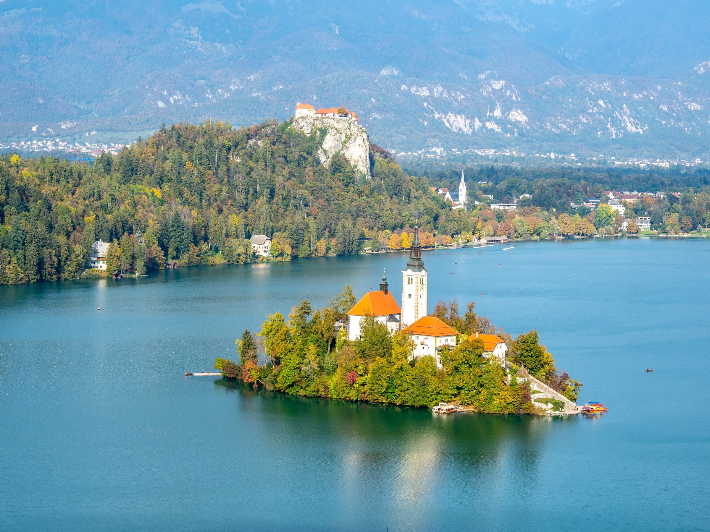 Pulau Bled dengan gereja beratap merah dan Kastil Bled di tebing, latar Pegunungan Alpen, Danau Bled, Slovenia