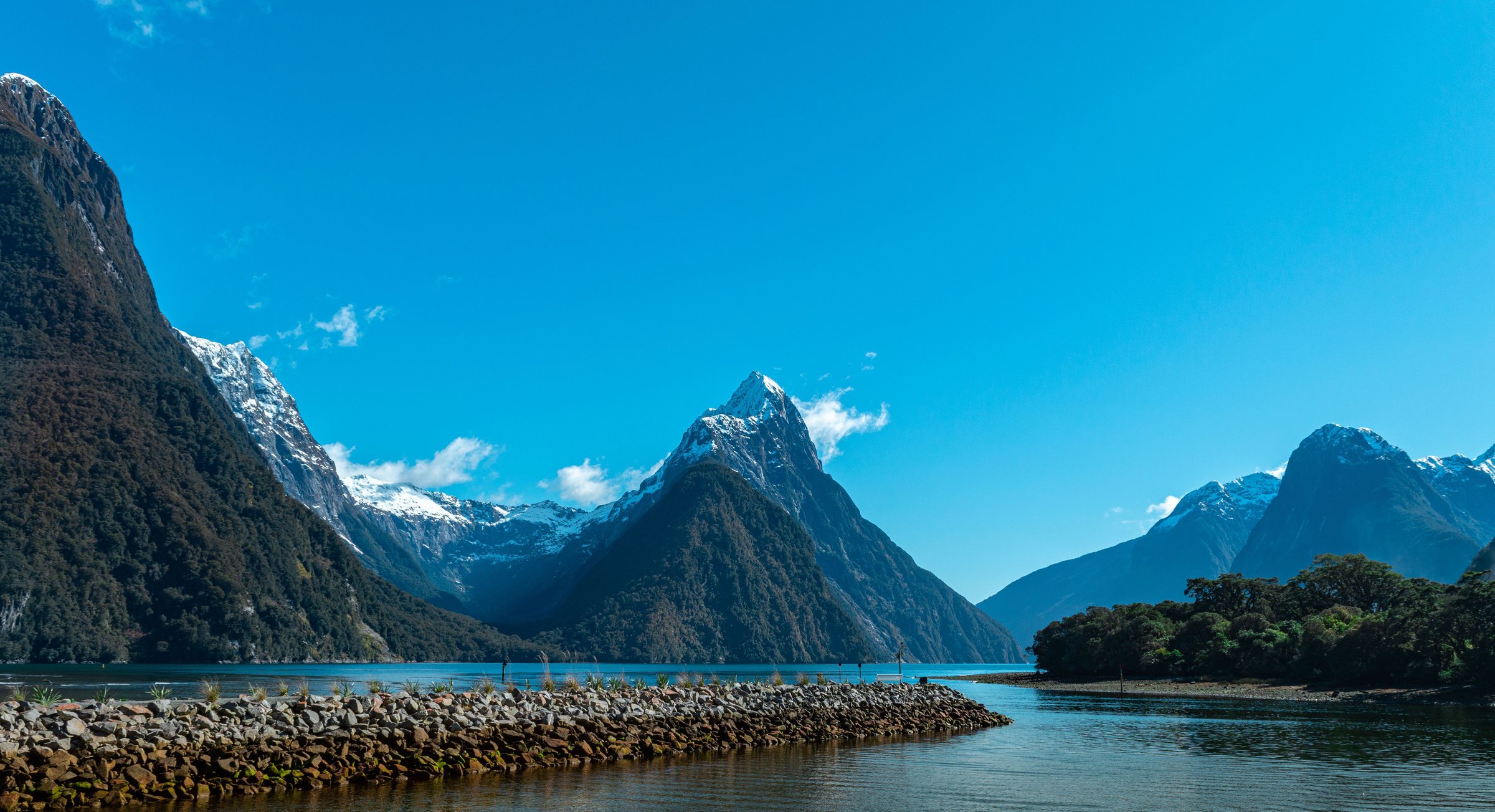 Mitre Peak menjulang tajam di atas perairan tenang Milford Sound dengan langit biru cerah