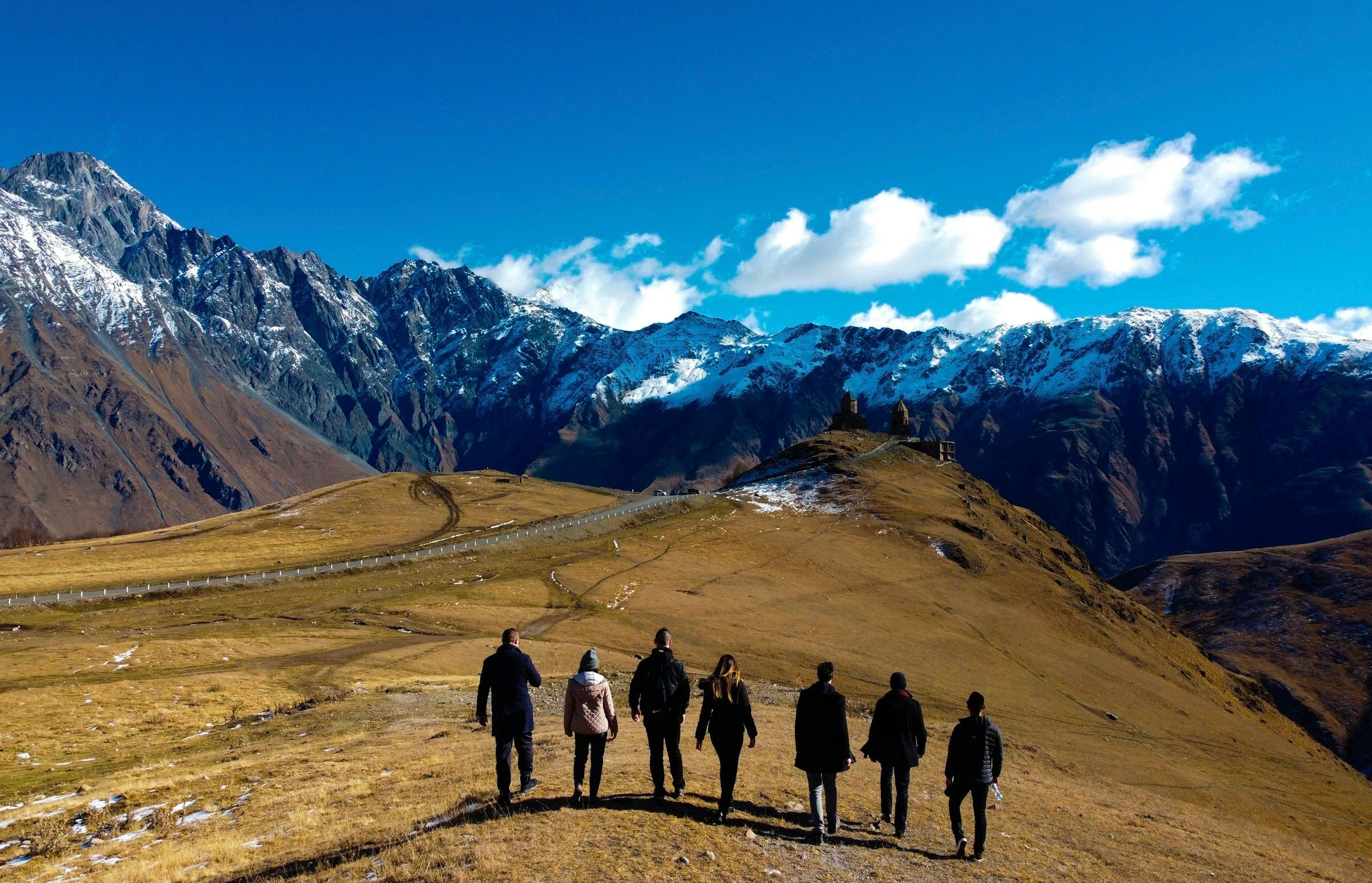 Sekelompok kecil wisatawan berjalan bersama menuju pegunungan bersalju, suasana tour grup kecil yang terkurasi