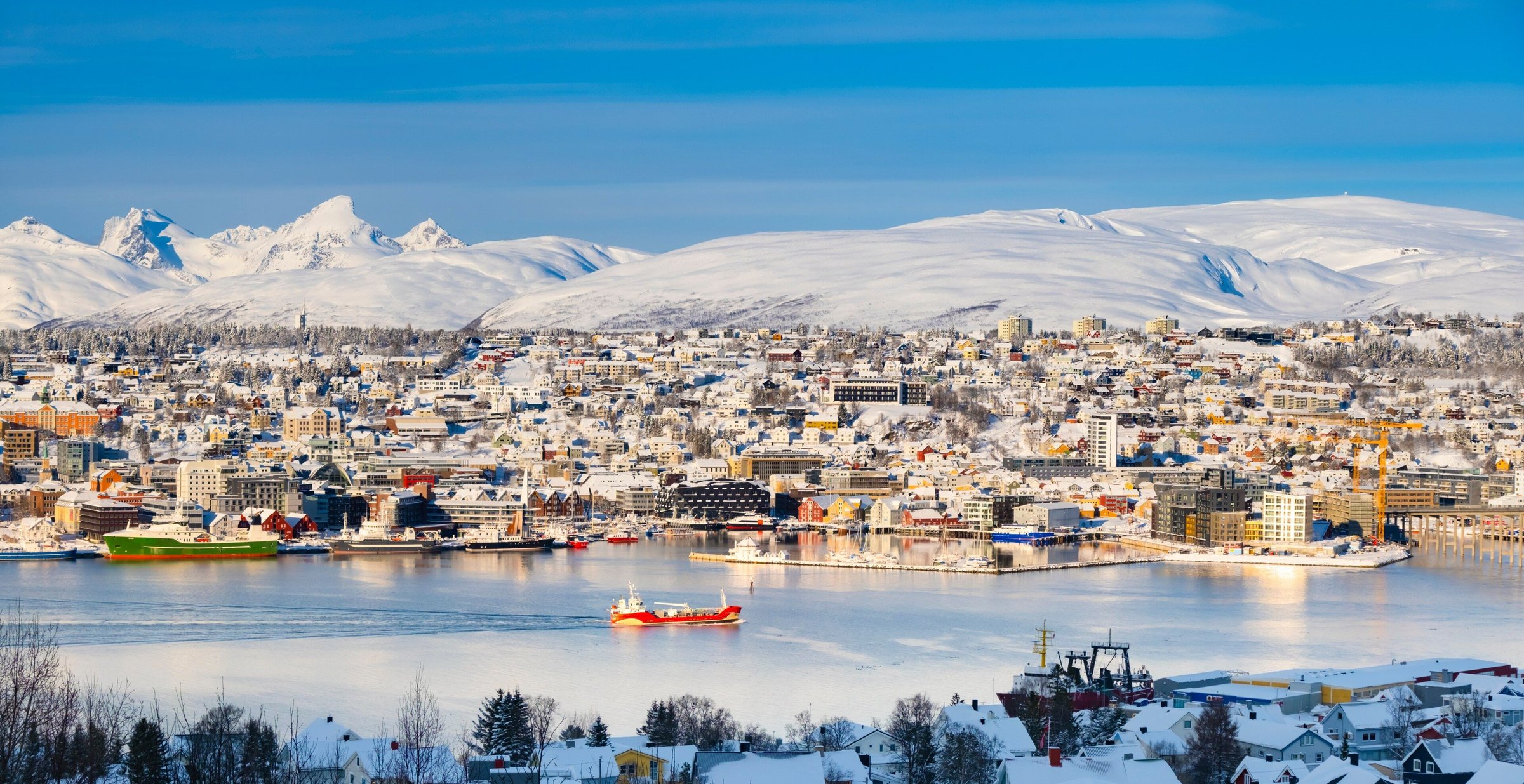 Kota Tromsø bersalju di tepi fjord dengan pegunungan putih di belakangnya.