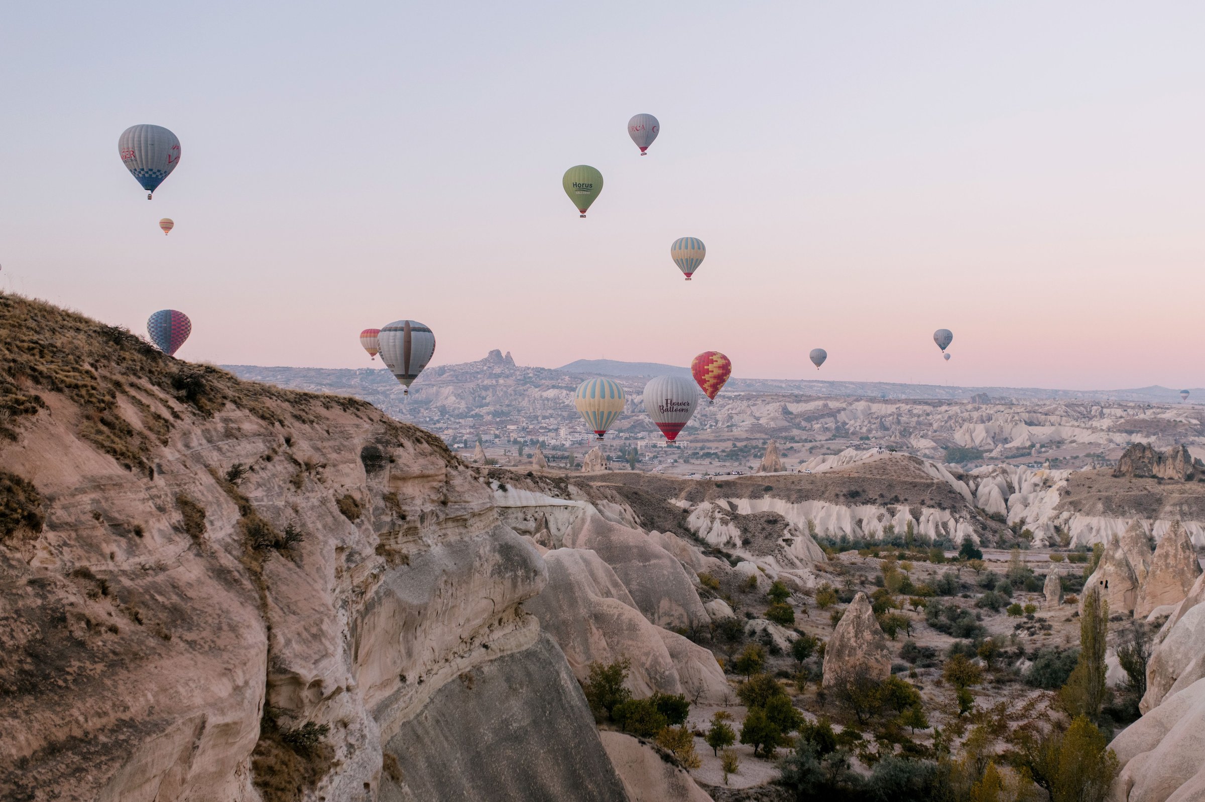 Balon udara warna-warni terbang di atas lembah batu Cappadocia saat fajar merah muda