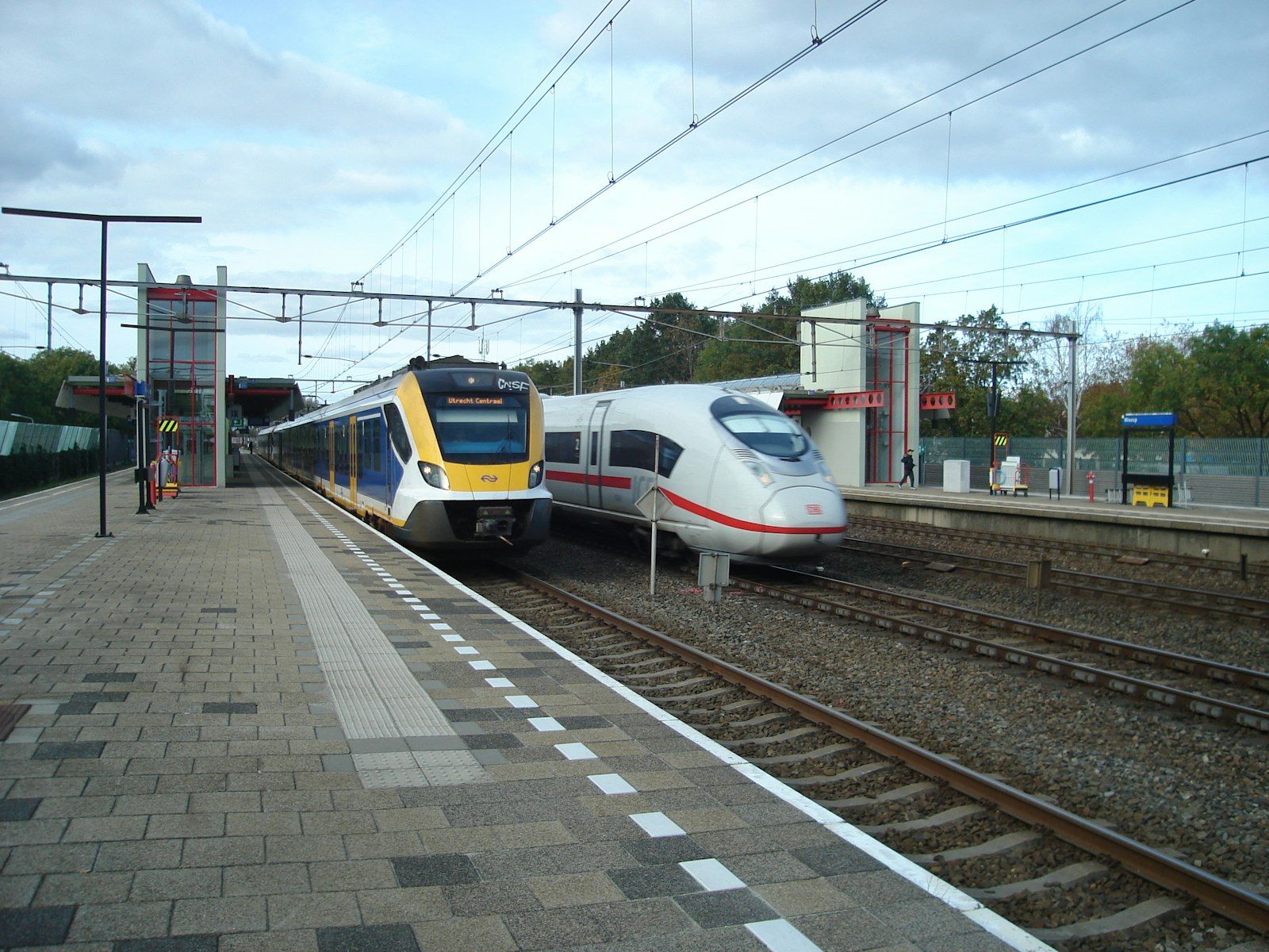 Kereta NS kuning biru dan ICE putih merah berdampingan di stasiun.
