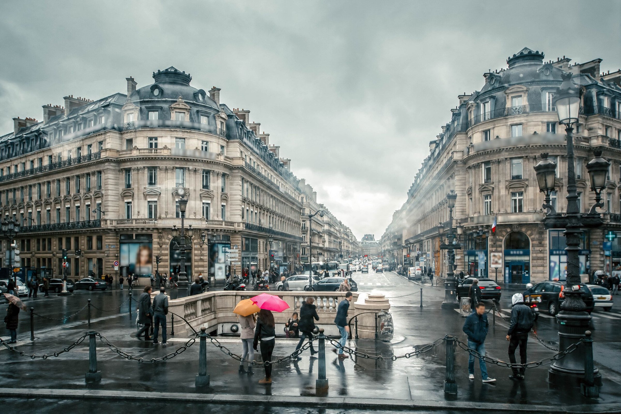Persimpangan jalan di pusat Paris dengan bangunan Haussmann dan pejalan kaki berpayung di hari berawan.