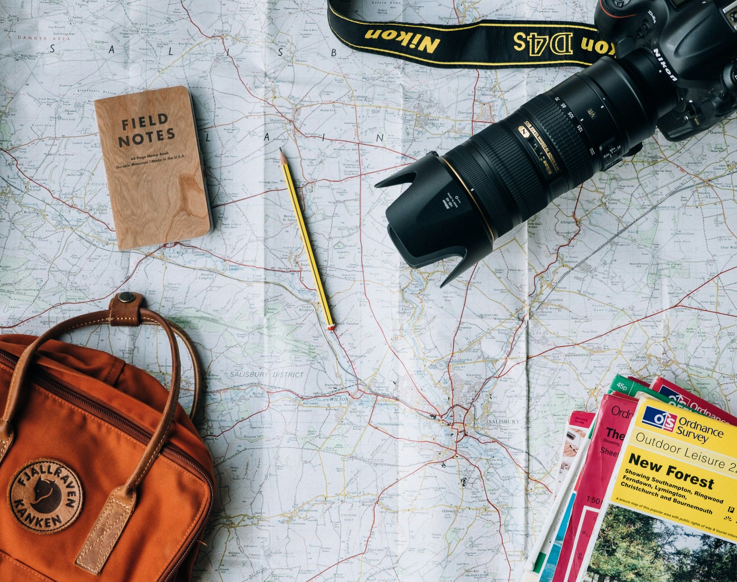 Peta, kamera, ransel, dan buku catatan tertata di atas meja — perlengkapan merencanakan perjalanan dan cuti