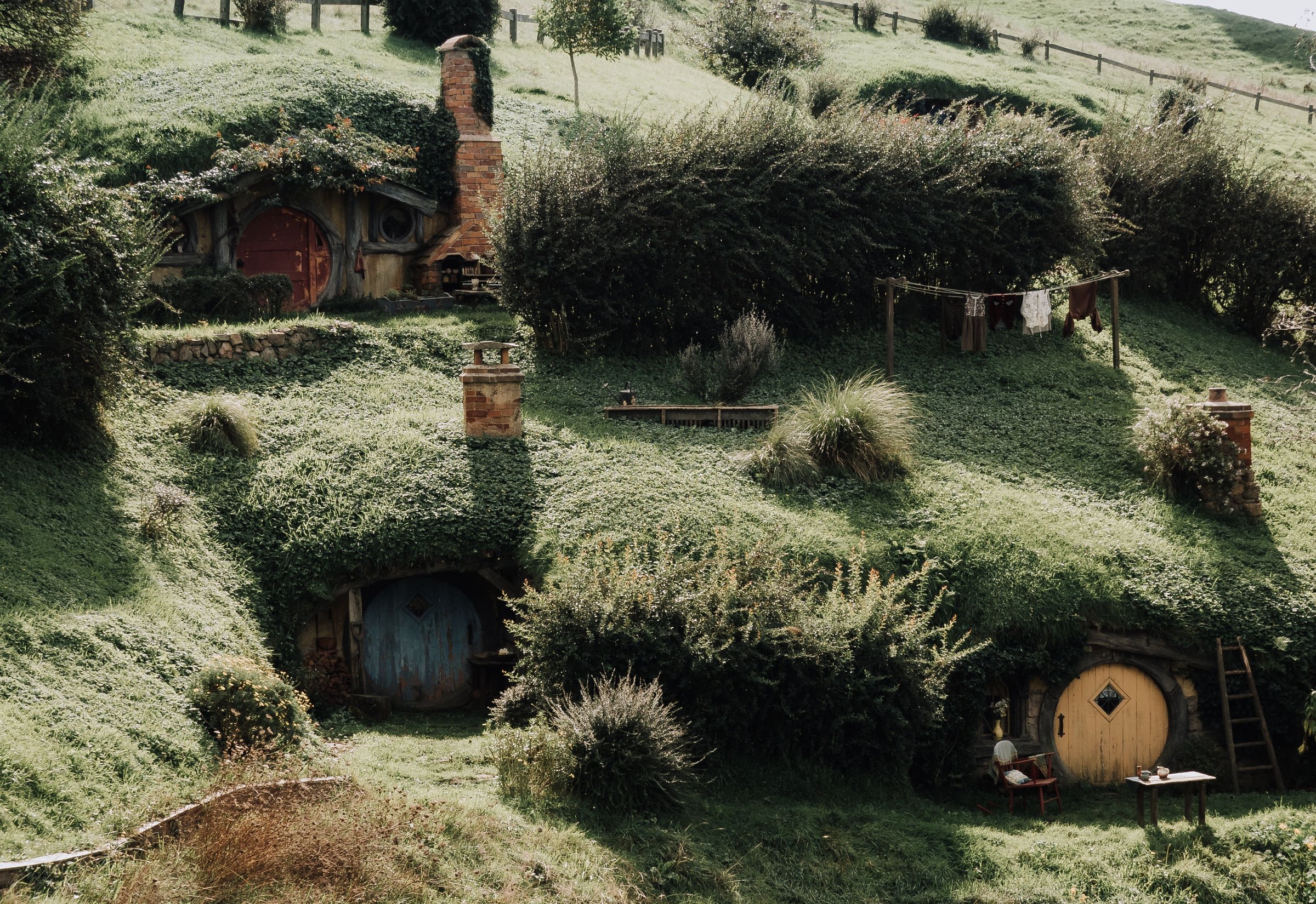 Tiga rumah hobbit bundar berpintu warna-warni di perbukitan hijau Hobbiton Movie Set