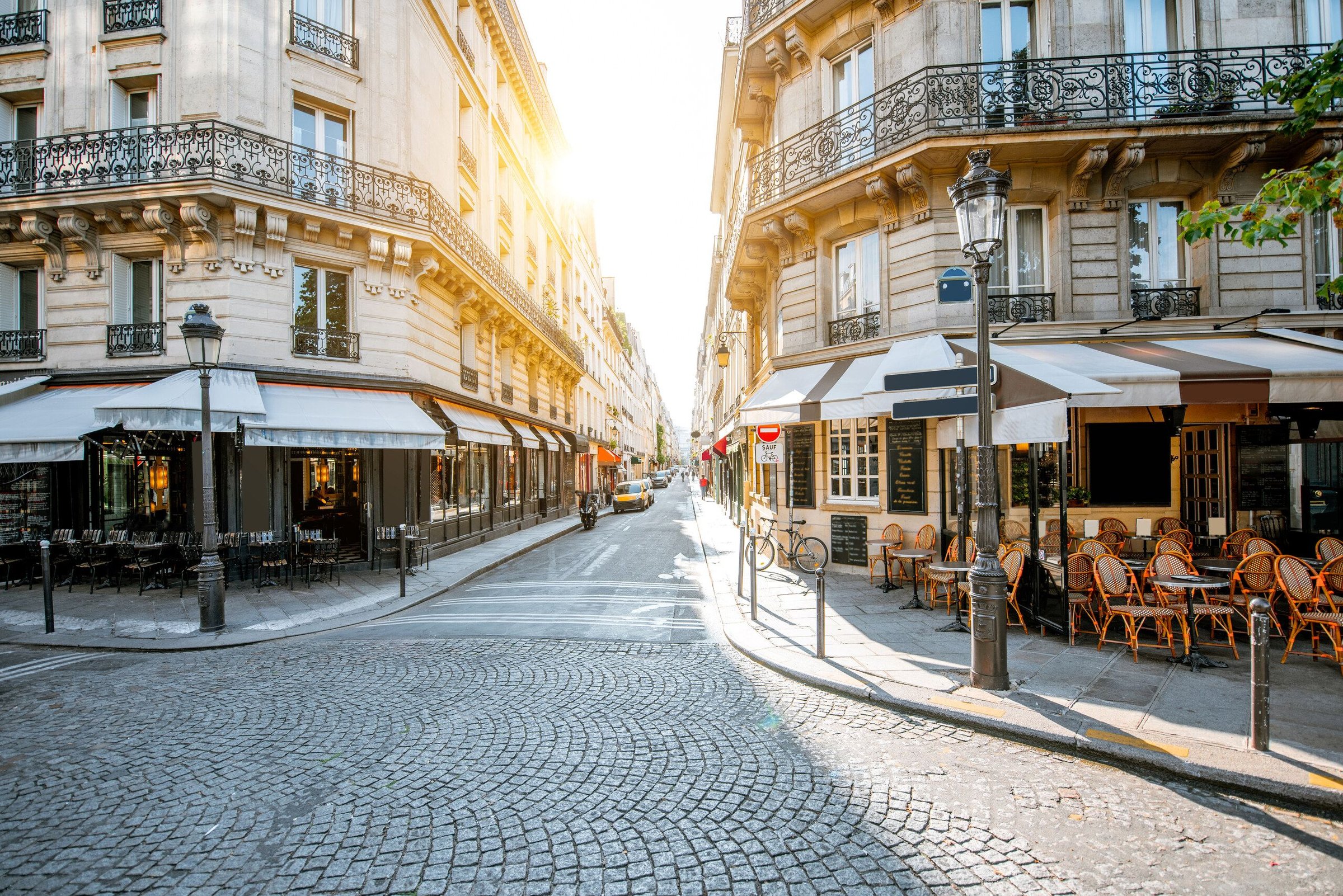 Jalan berbatu di Paris dengan kafe teras dan bangunan khas yang diterangi cahaya pagi.