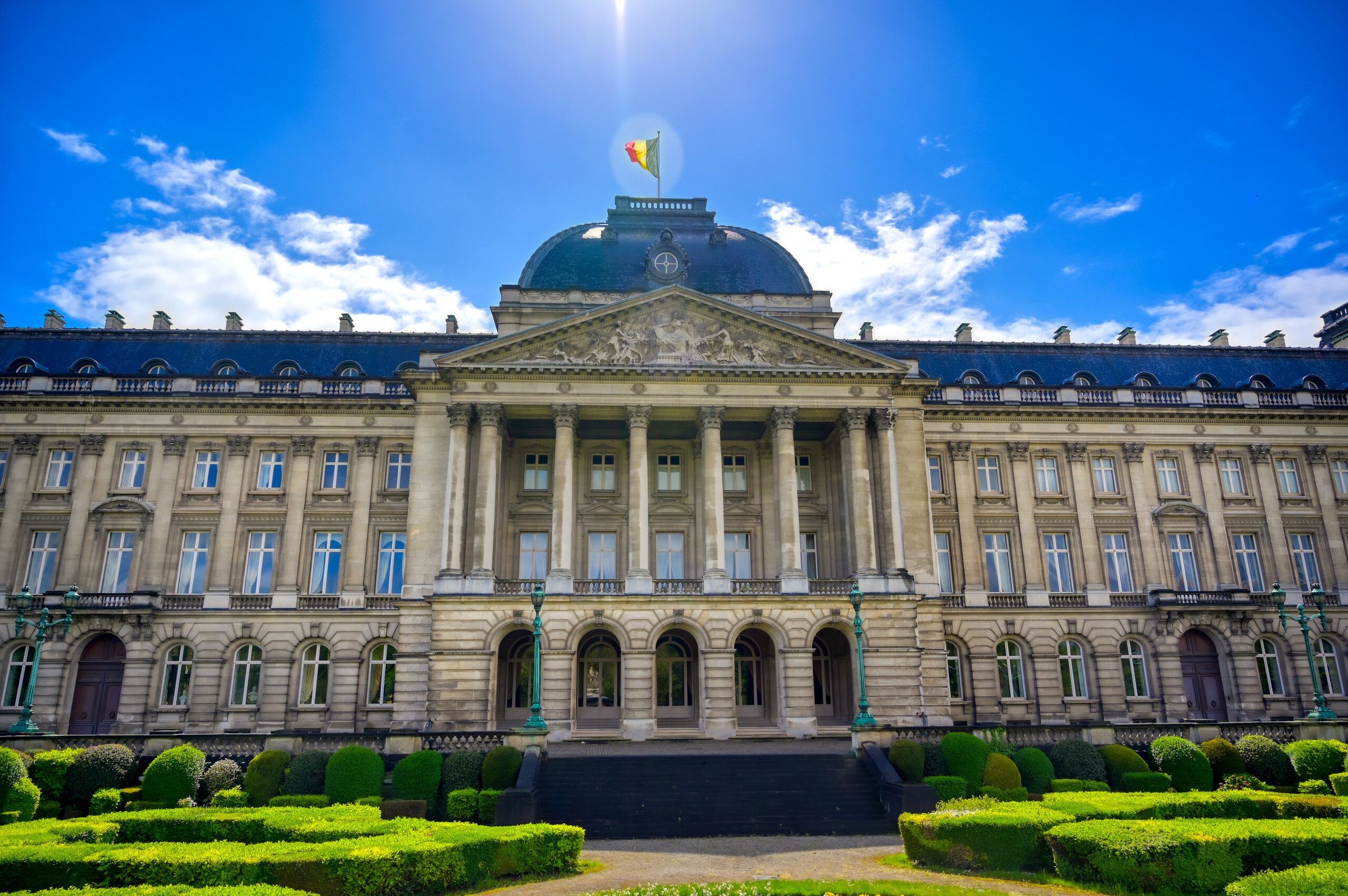 Royal Palace Brussels dengan taman rapi dan bendera di atap pada hari cerah.
