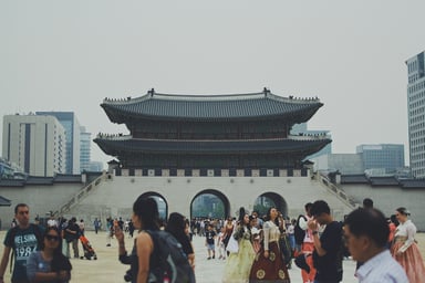 Gerbang Gwanghwamun Istana Gyeongbokgung di Seoul dengan pengunjung berhanbok dan latar gedung kota