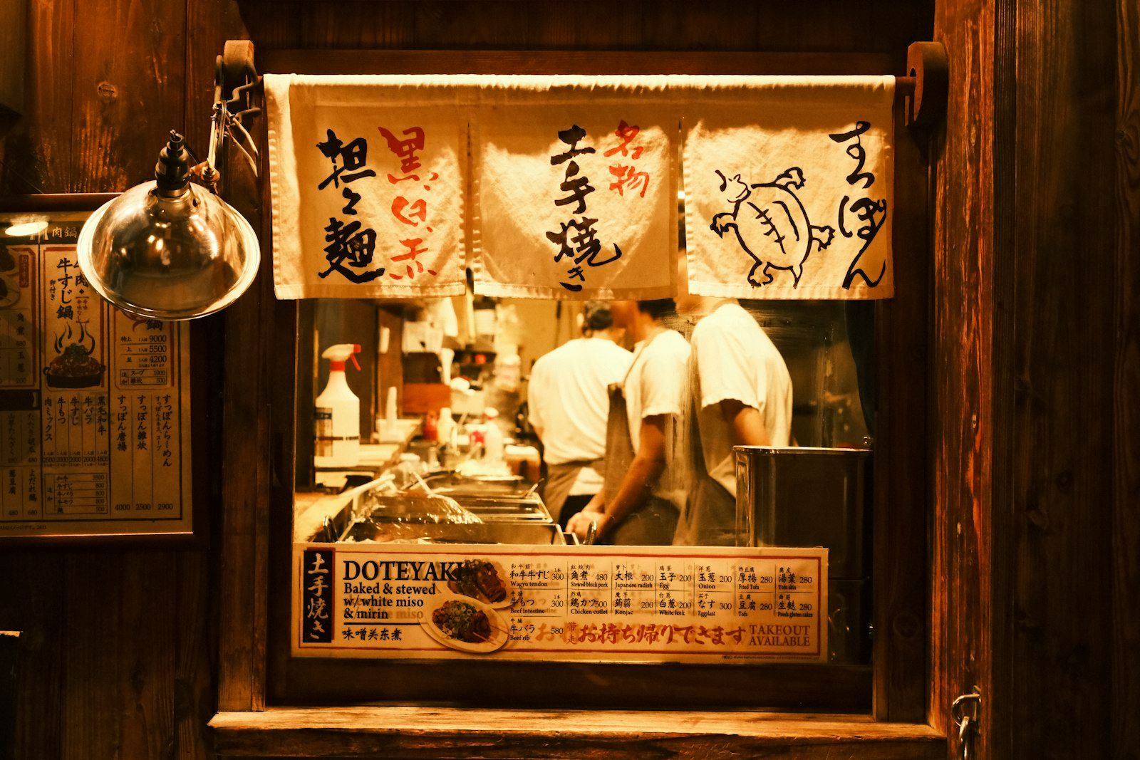 Pintu masuk kedai Jepang berbingkai kayu dengan noren, menu Doteyaki, dan koki di dalam.