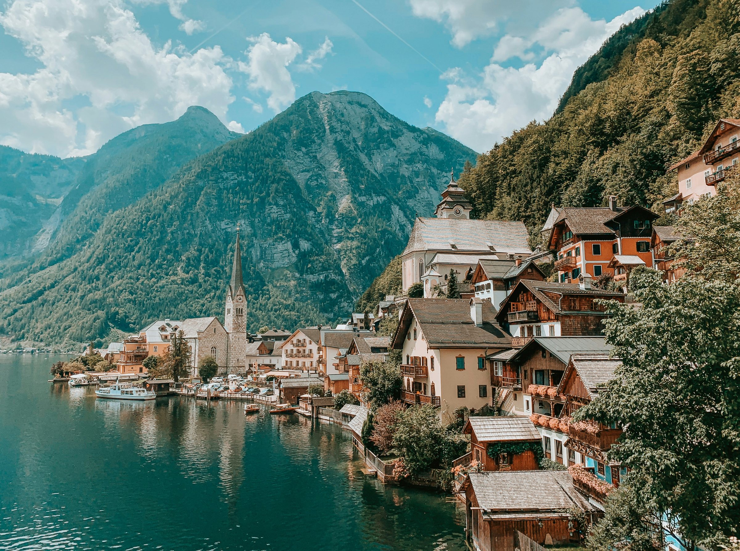 Desa Hallstatt di tepi danau dengan menara gereja dan rumah kayu bergaya Alpen di kaki pegunungan, Austria