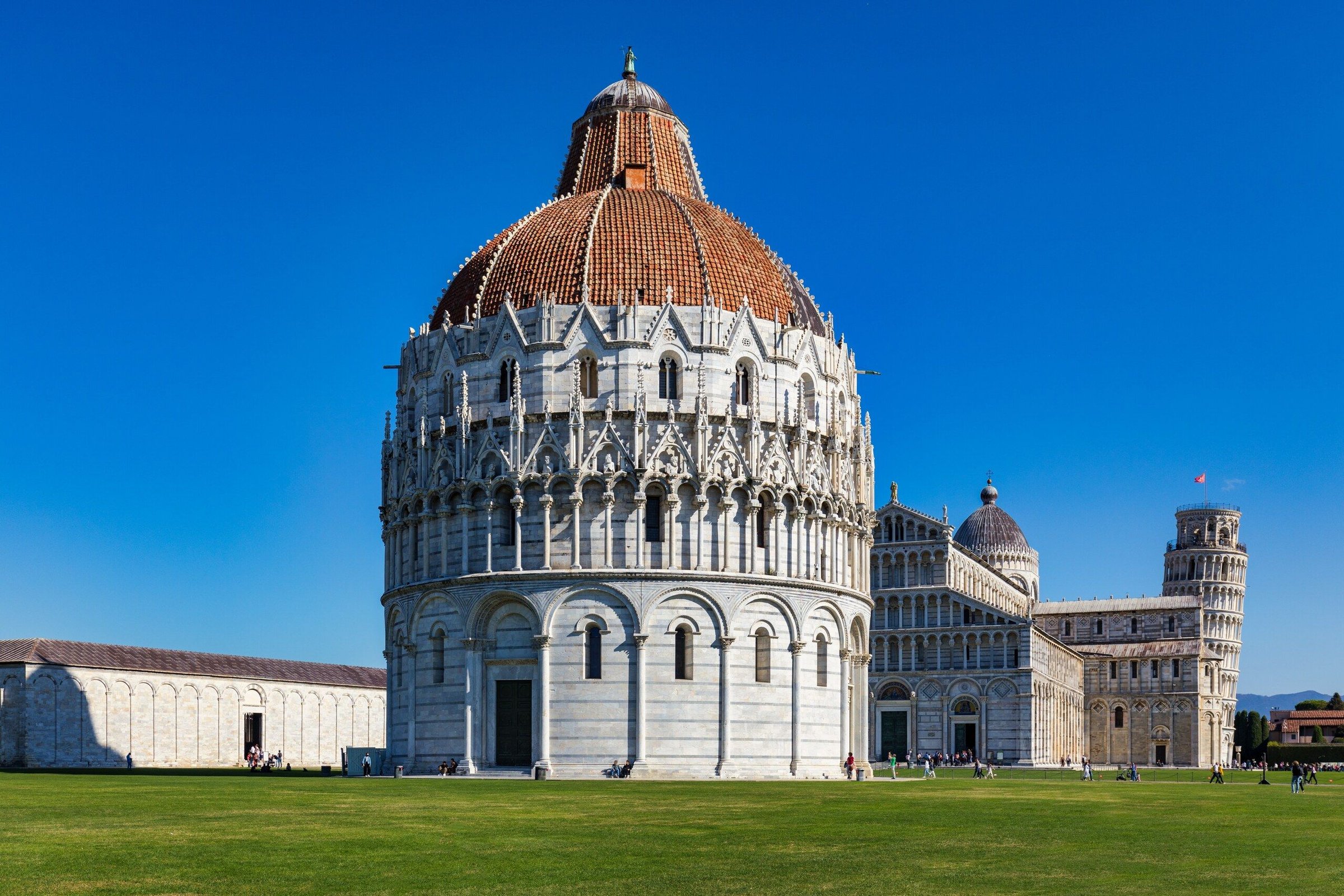 Katedral Pisa dan Menara Miring di Piazza dei Miracoli pada hari cerah dengan rumput hijau.