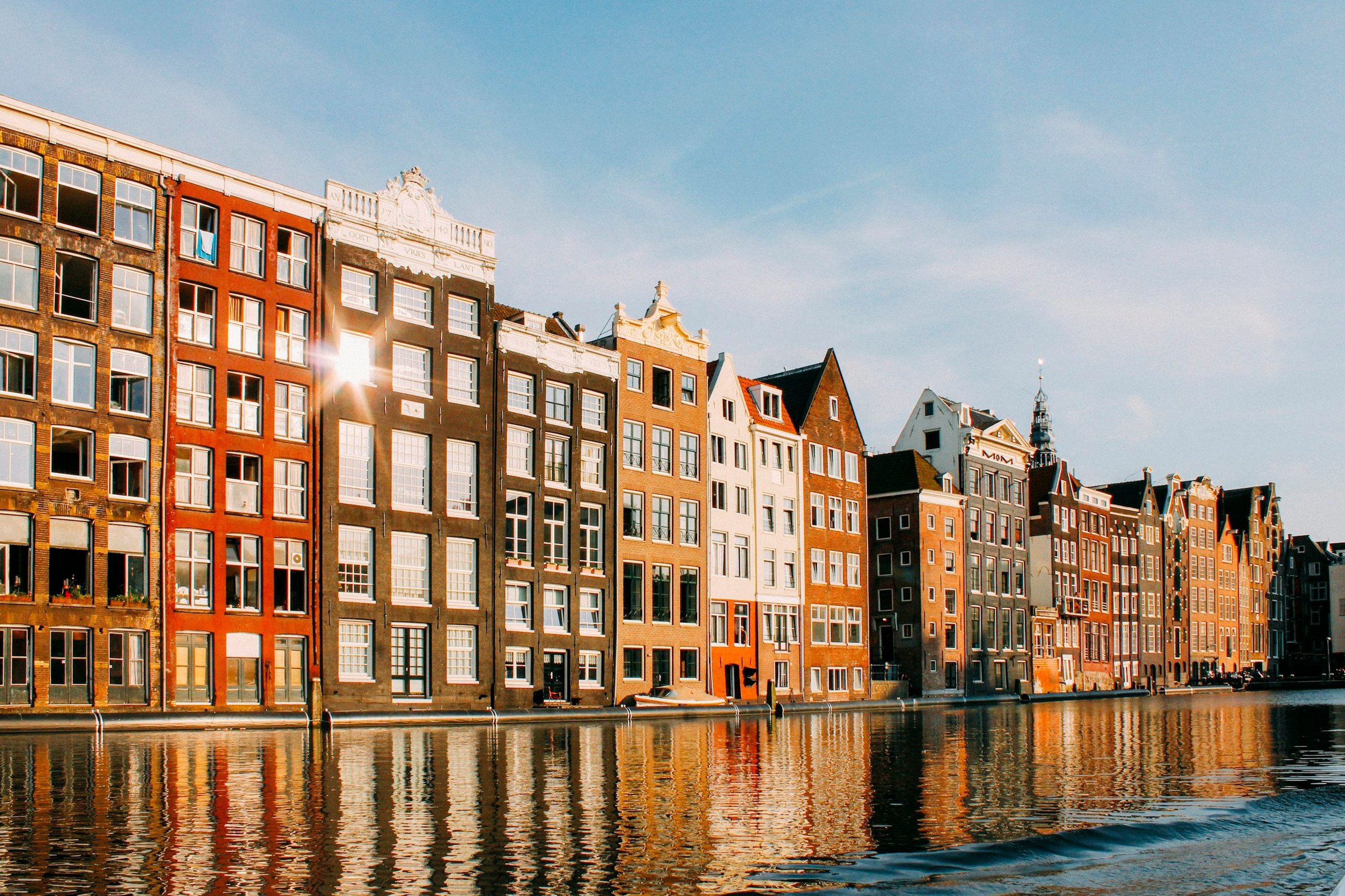 Deretan rumah kanal Amsterdam berwarna-warni terpantul di air saat cahaya keemasan sore