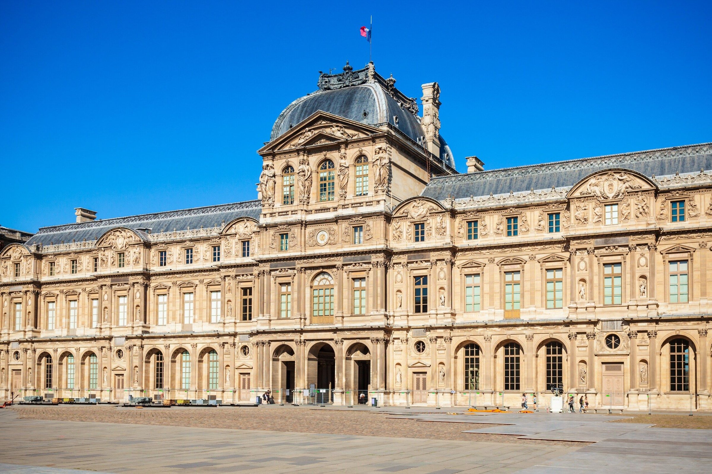 Bangunan Museum Louvre di Paris dari halaman dalam di bawah langit biru cerah.