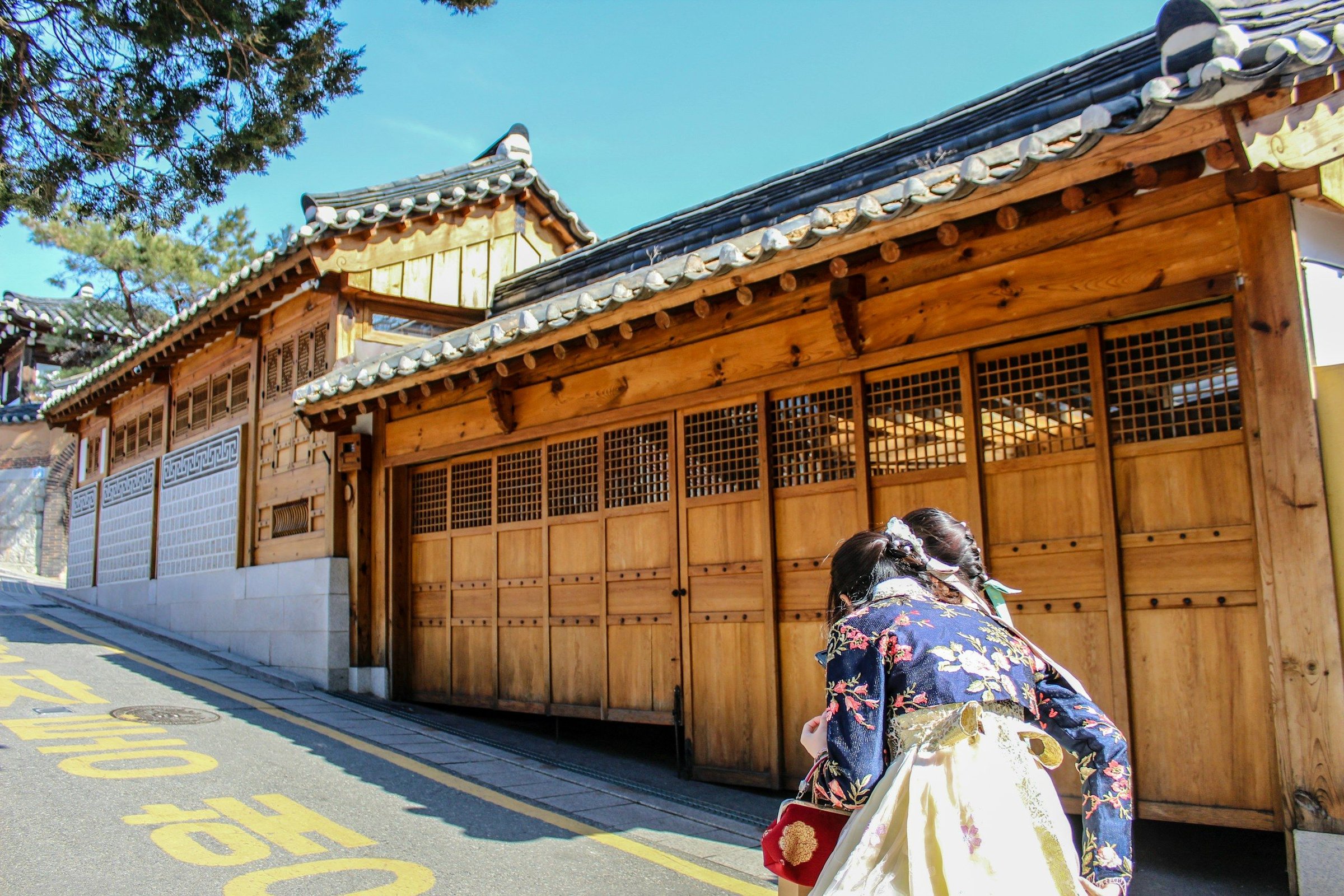 Perempuan mengenakan hanbok berjalan di depan bangunan hanok kayu tradisional Korea