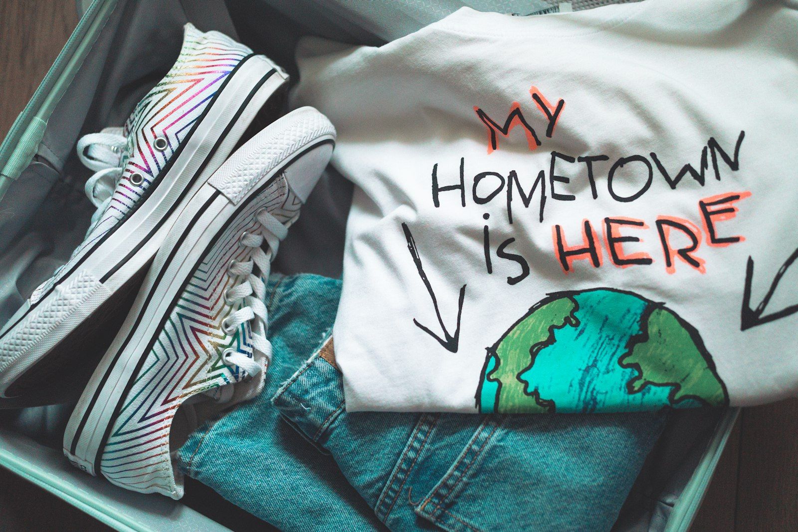 Sepatu kets berwarna-warni, kaus "MY HOMETOWN IS HERE", dan celana jins di koper.