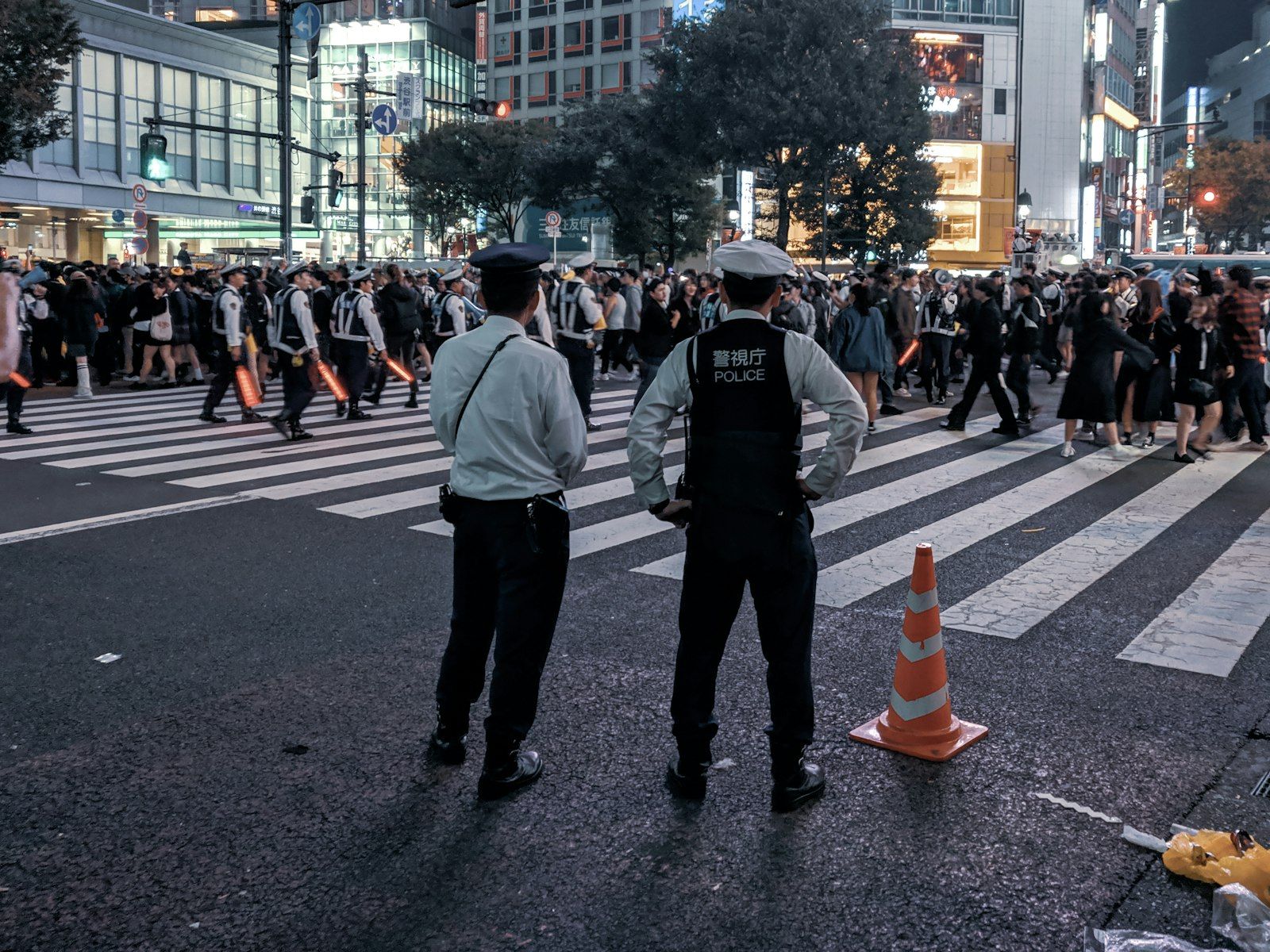 Dua polisi Jepang mengawasi pejalan kaki di penyeberangan jalan kota yang ramai.