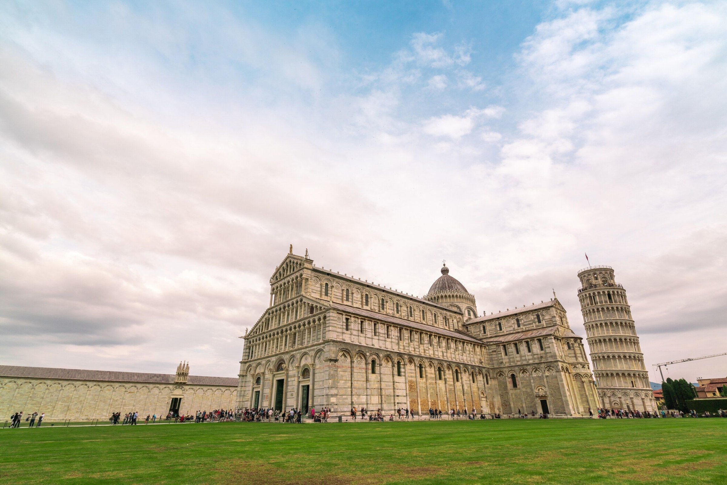 Menara Miring Pisa dan Duomo di Piazza dei Miracoli saat senja, dengan rumput hijau di depannya.