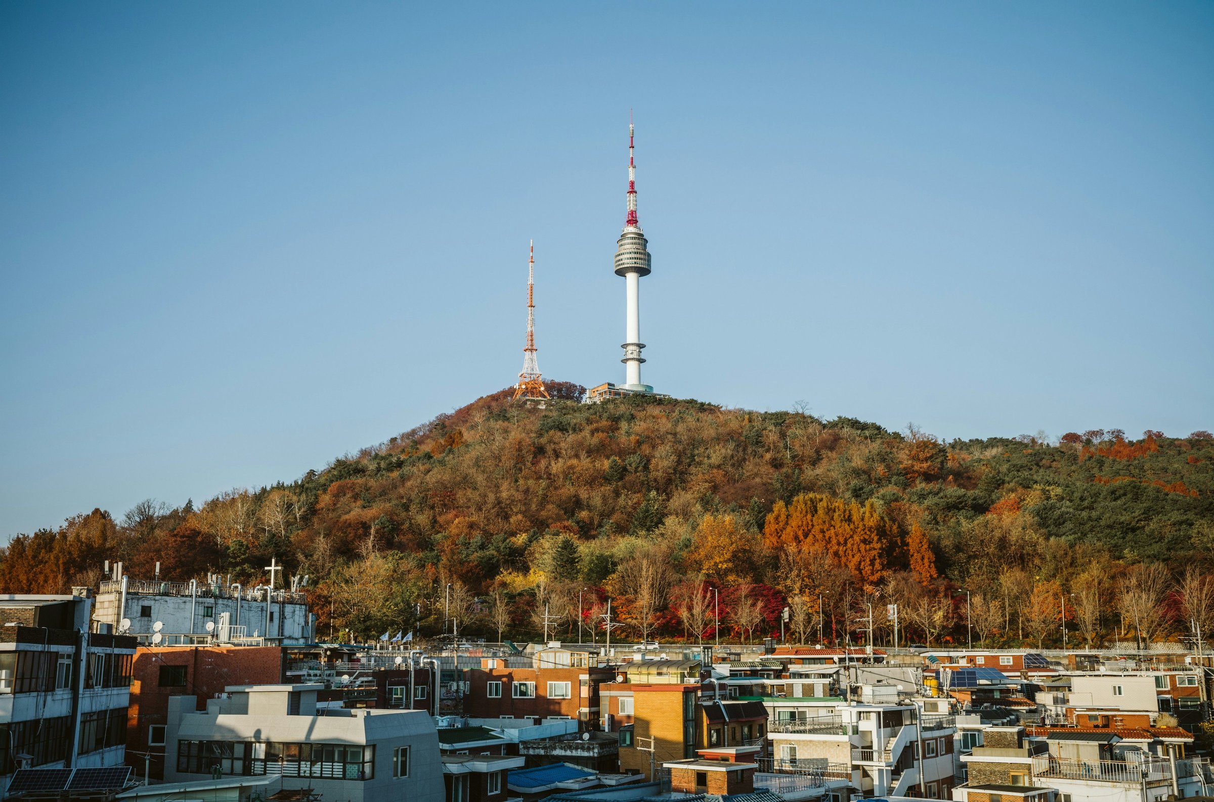Panorama Seoul dari ketinggian dengan pepohonan musim gugur di lereng bukit.