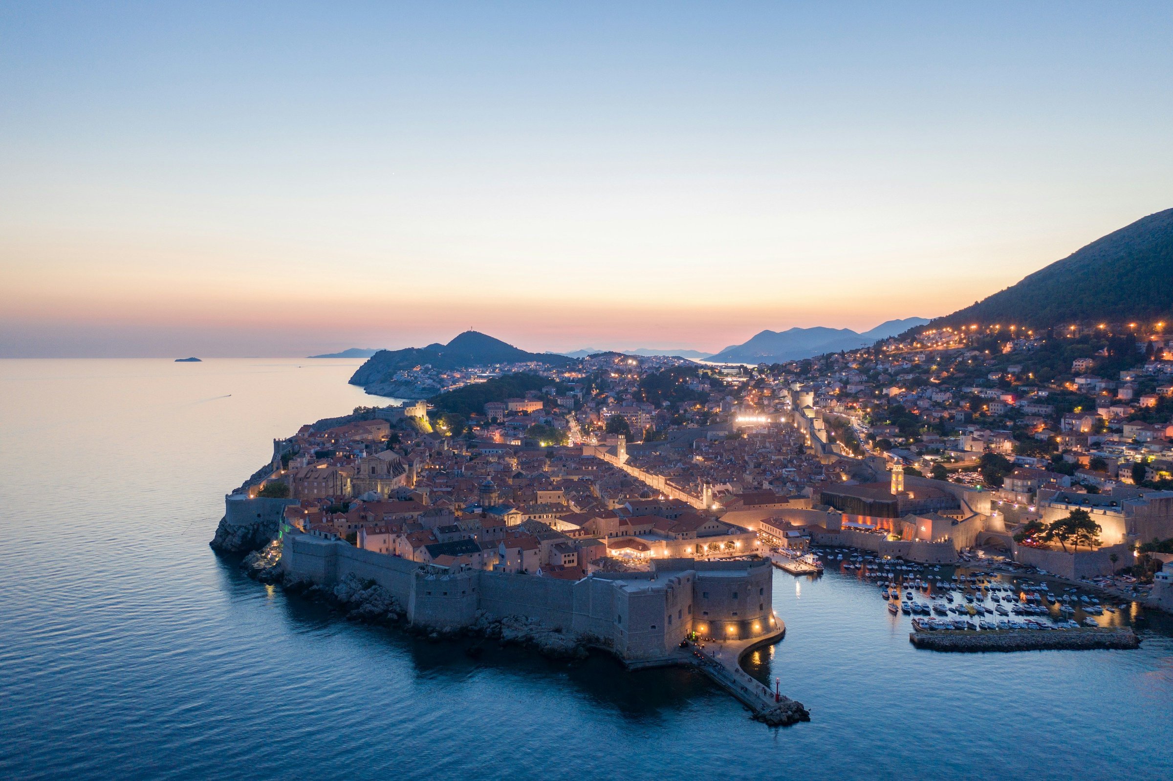 Kota tua Dubrovnik berdinding di tepi Laut Adriatik saat biru senja, dilihat dari udara.