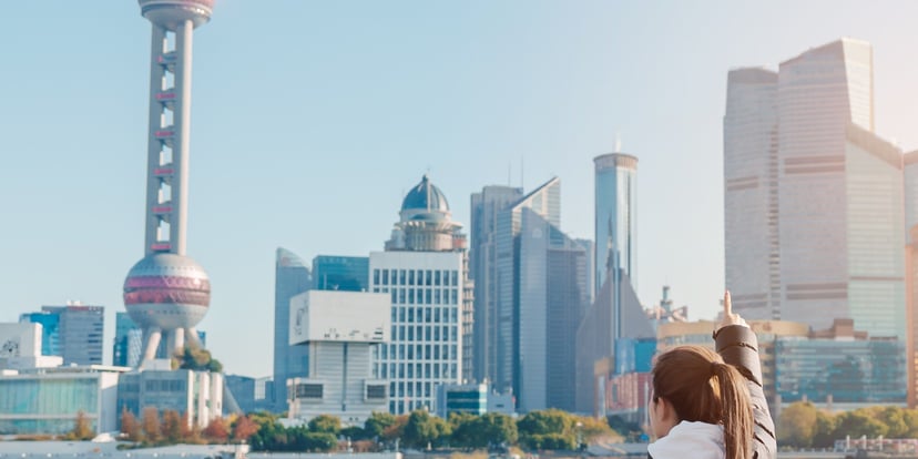 Perempuan berjaket memandang skyline Pudong dan Oriental Pearl Tower dari tepi sungai The Bund, Shanghai, siang cerah