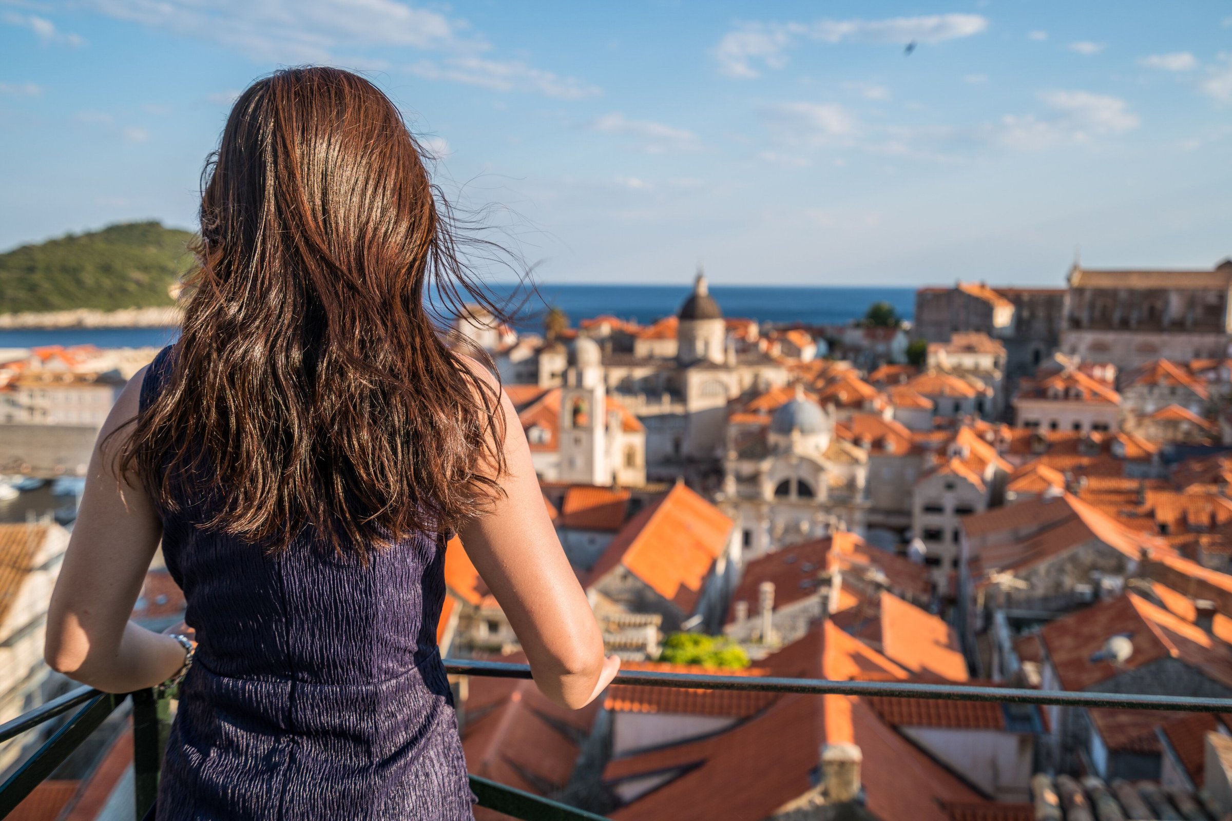 Perempuan memandang atap oranye kota tua Dubrovnik dari tembok kota