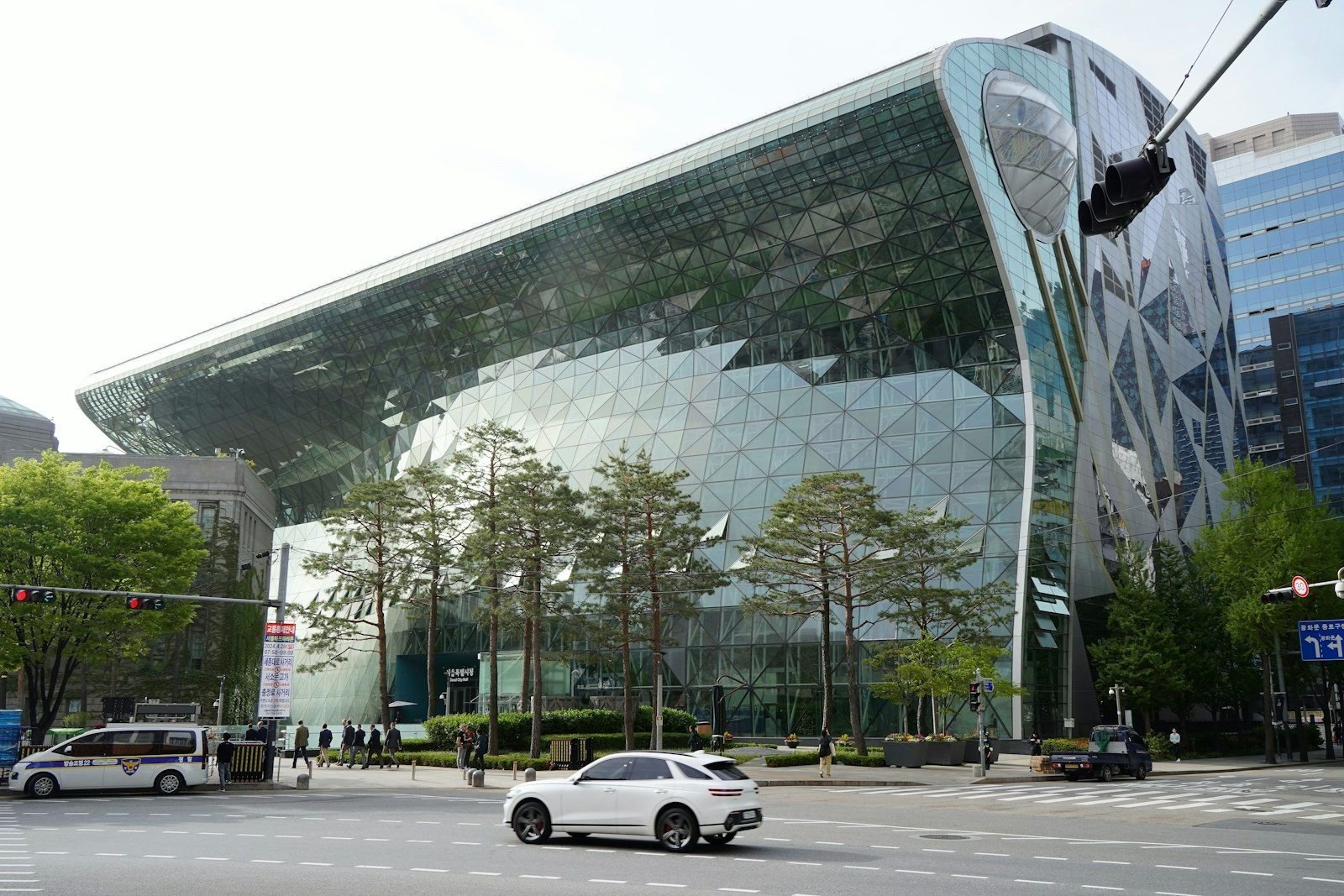Gedung kaca modern melengkung dengan panel geometris di jalan kota yang ramai.