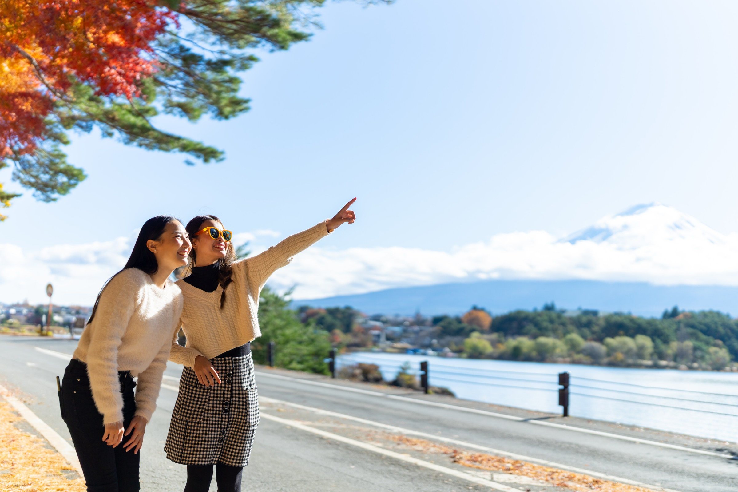 Dua perempuan menunjuk Gunung Fuji di tepi Danau Kawaguchi dengan daun merah