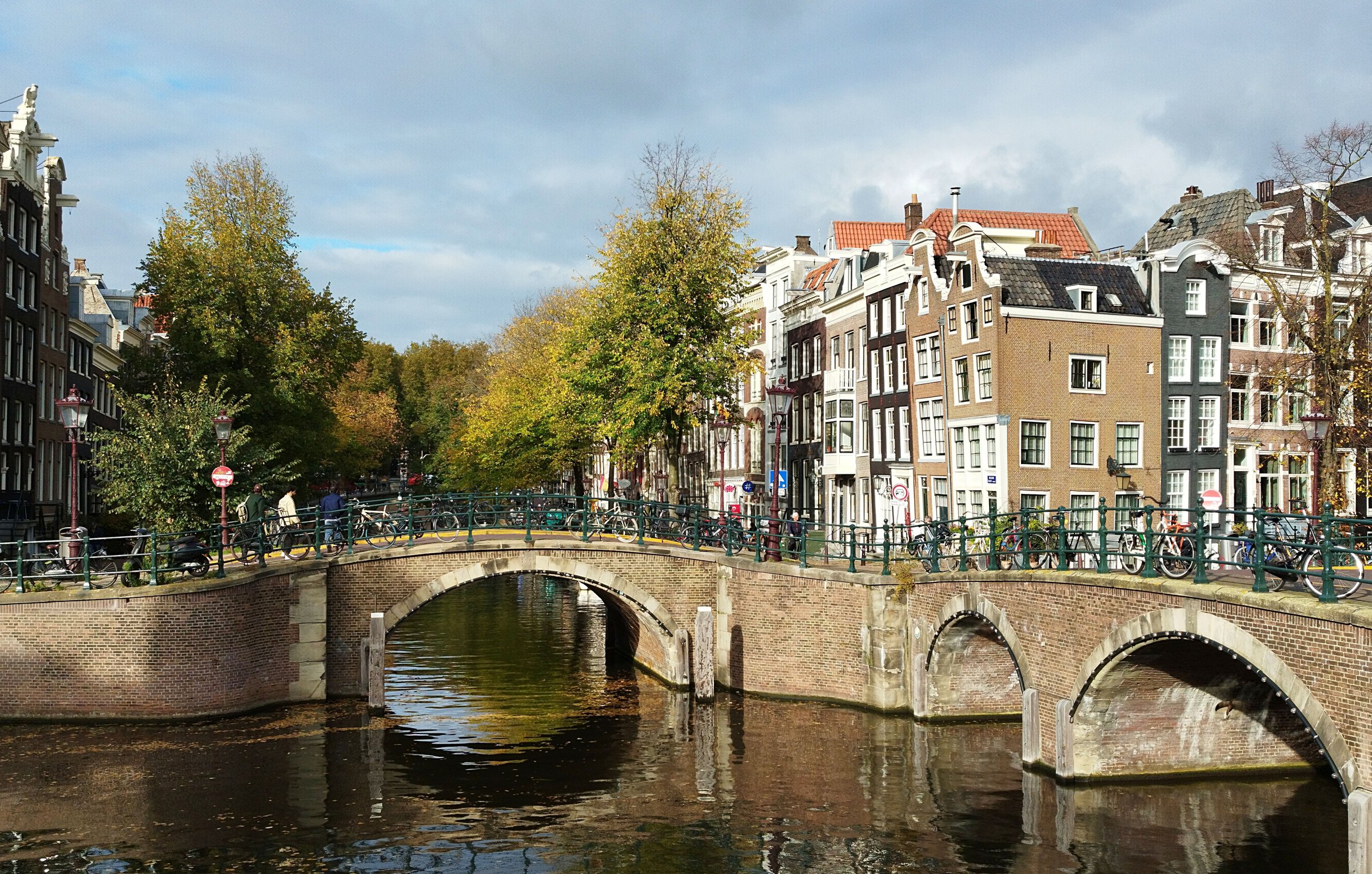 Jembatan batu bersejarah di atas kanal Amsterdam dikelilingi rumah bergaya gable klasik