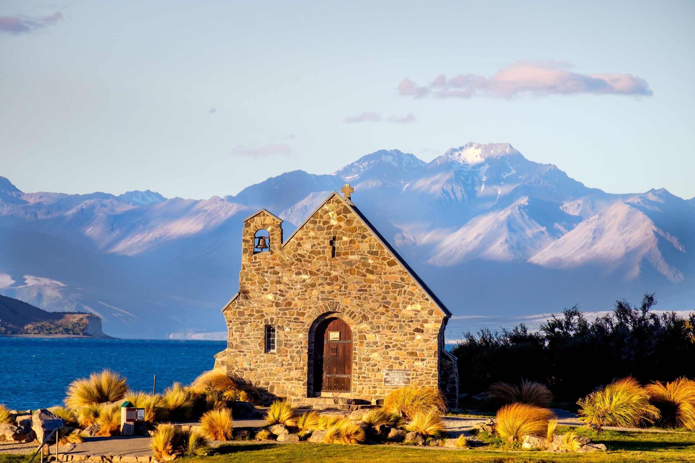 Church of the Good Shepherd dari batu di tepi Lake Tekapo yang biru dengan pegunungan bersalju