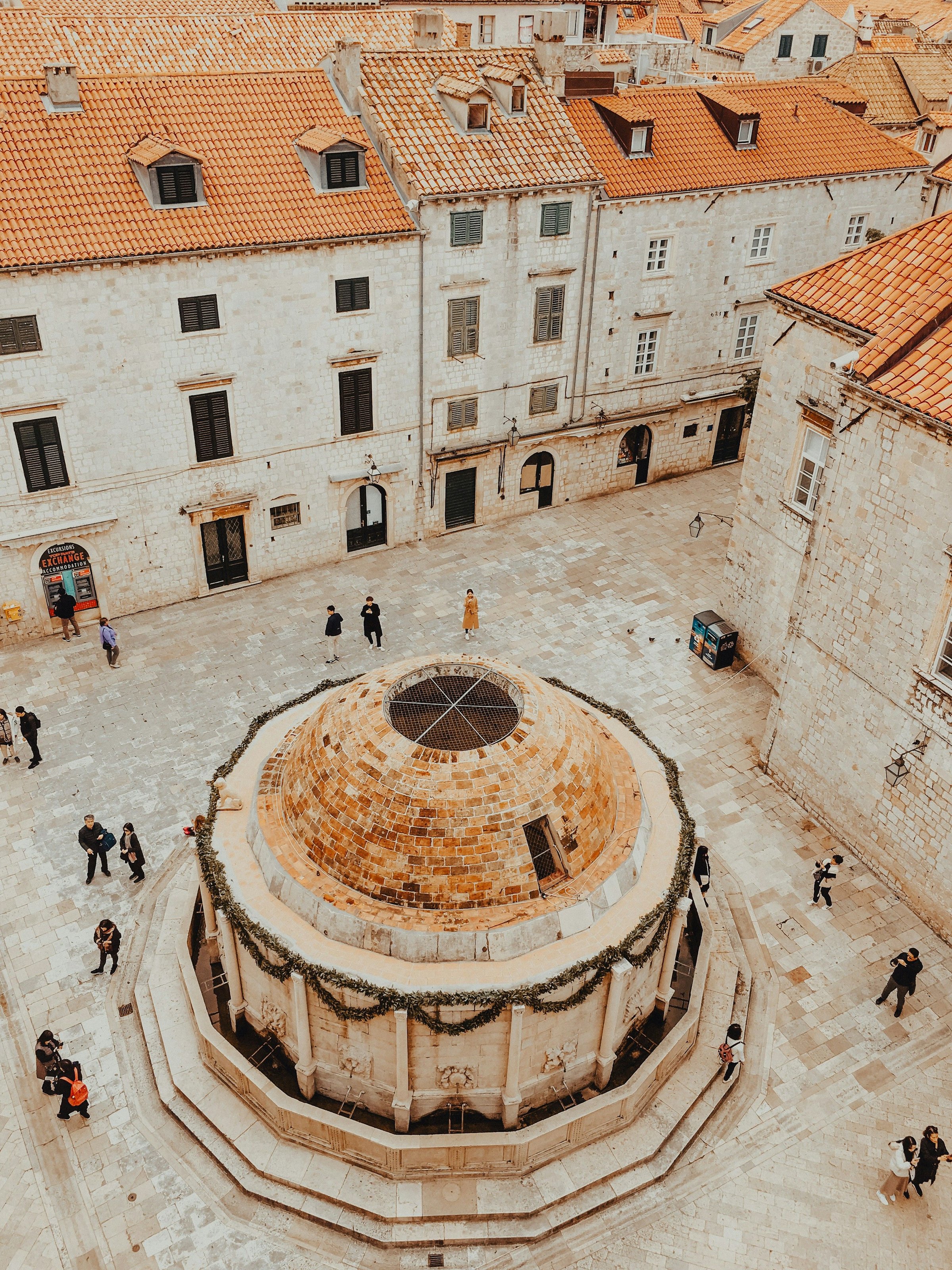 Alun-alun batu kota tua Dubrovnik dengan air mancur berkubah dan atap terakota di sekelilingnya.