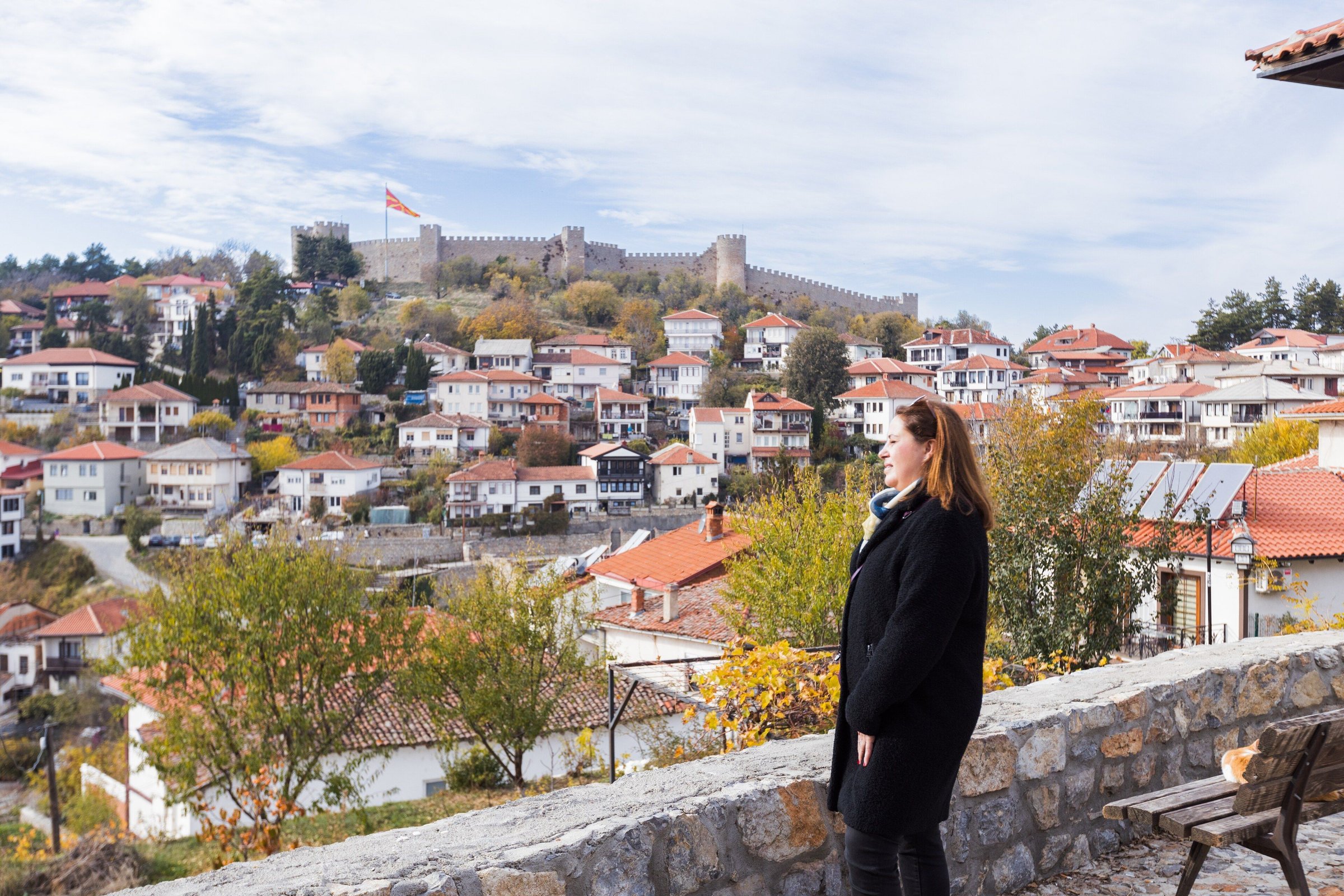 Perempuan berjaket memandang kota Ohrid dengan dedaunan musim gugur dan Danau Ohrid