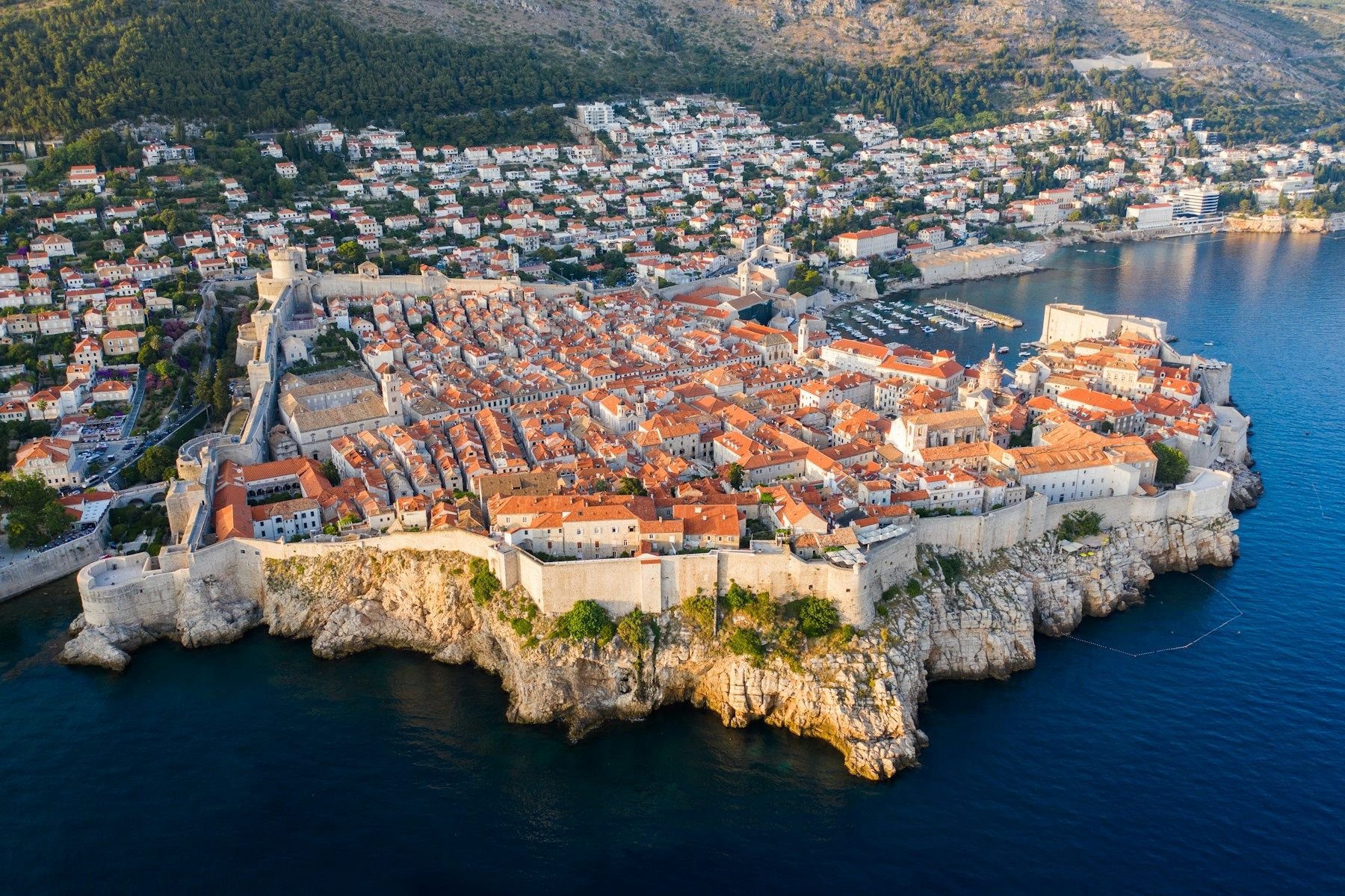 Tembok kota Dubrovnik dari atas, dengan Laut Adriatik biru tua dan atap oranye Old Town yang ikonik