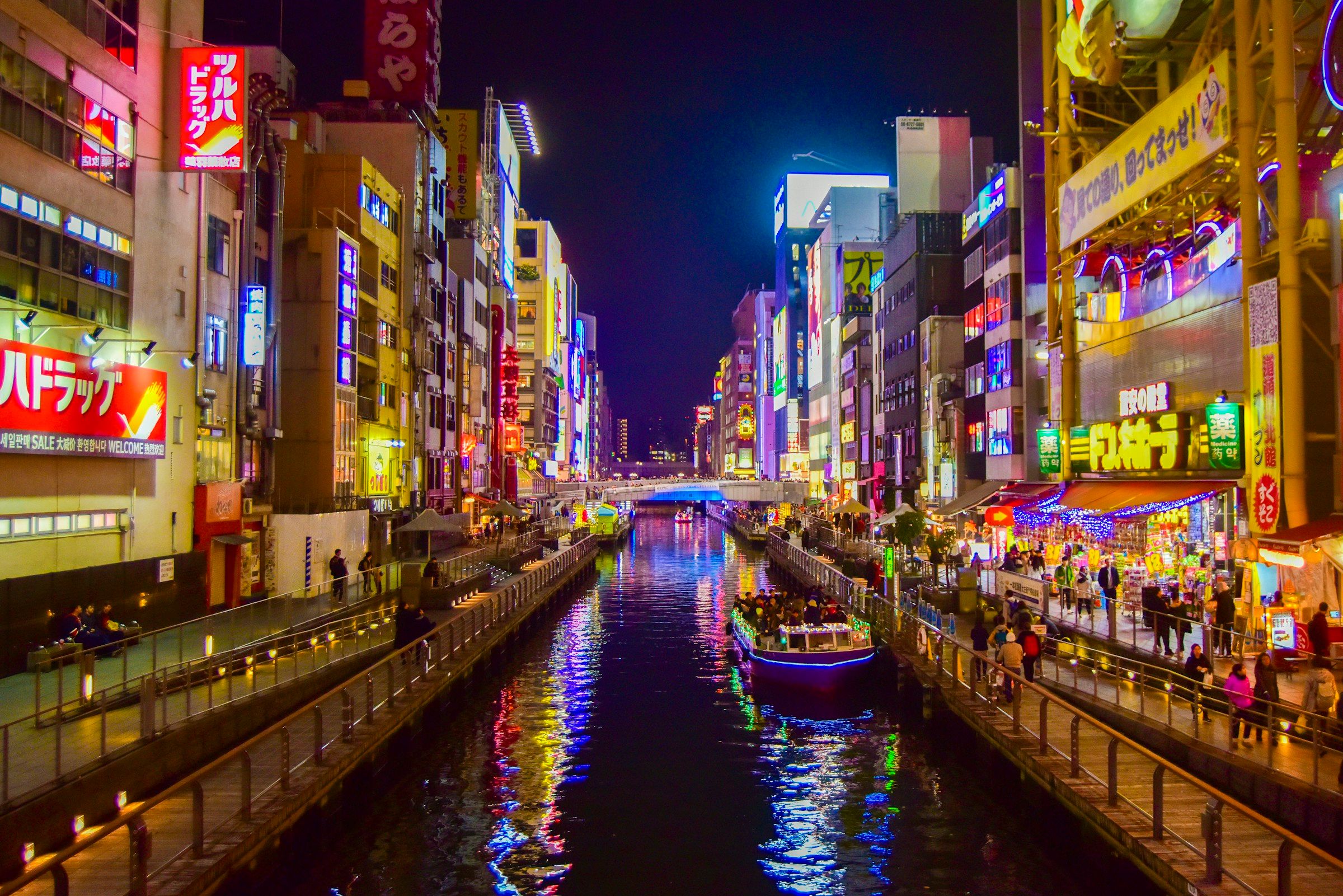 Kanal Dotonbori malam hari dengan pantulan neon di air dan perahu menyusuri kanal, Osaka