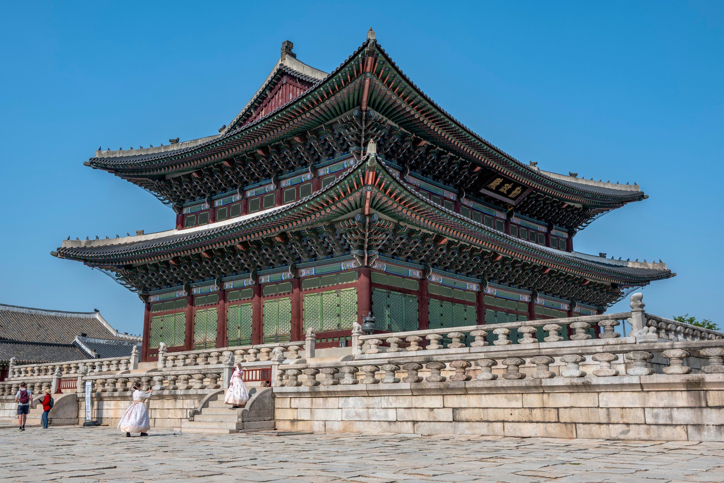 Balairung utama Istana Gyeongbokgung dengan pengunjung berhanbok putih di langit biru cerah