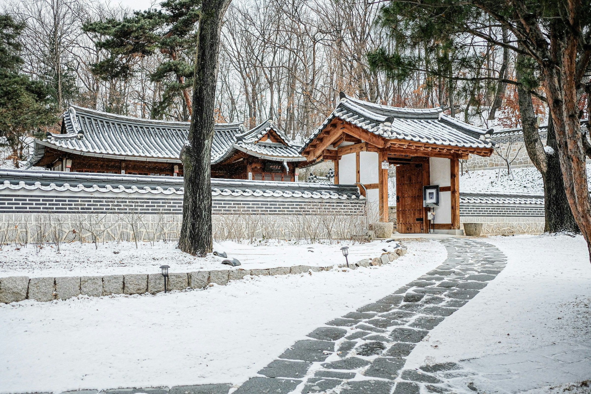 Hanok tradisional Korea bersalju dengan gerbang kayu dan jalan batu tertutup salju