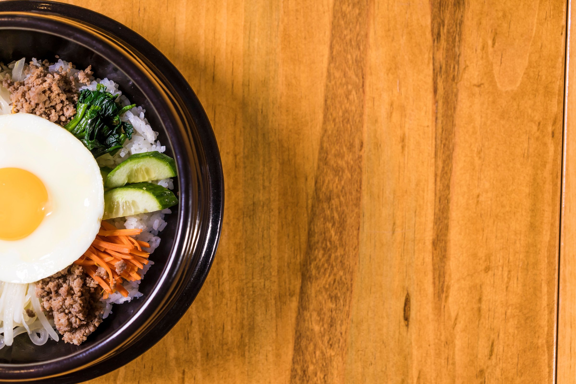Semangkuk bibimbap Korea dengan telur mata sapi, sayuran segar, dan daging di atas meja kayu
