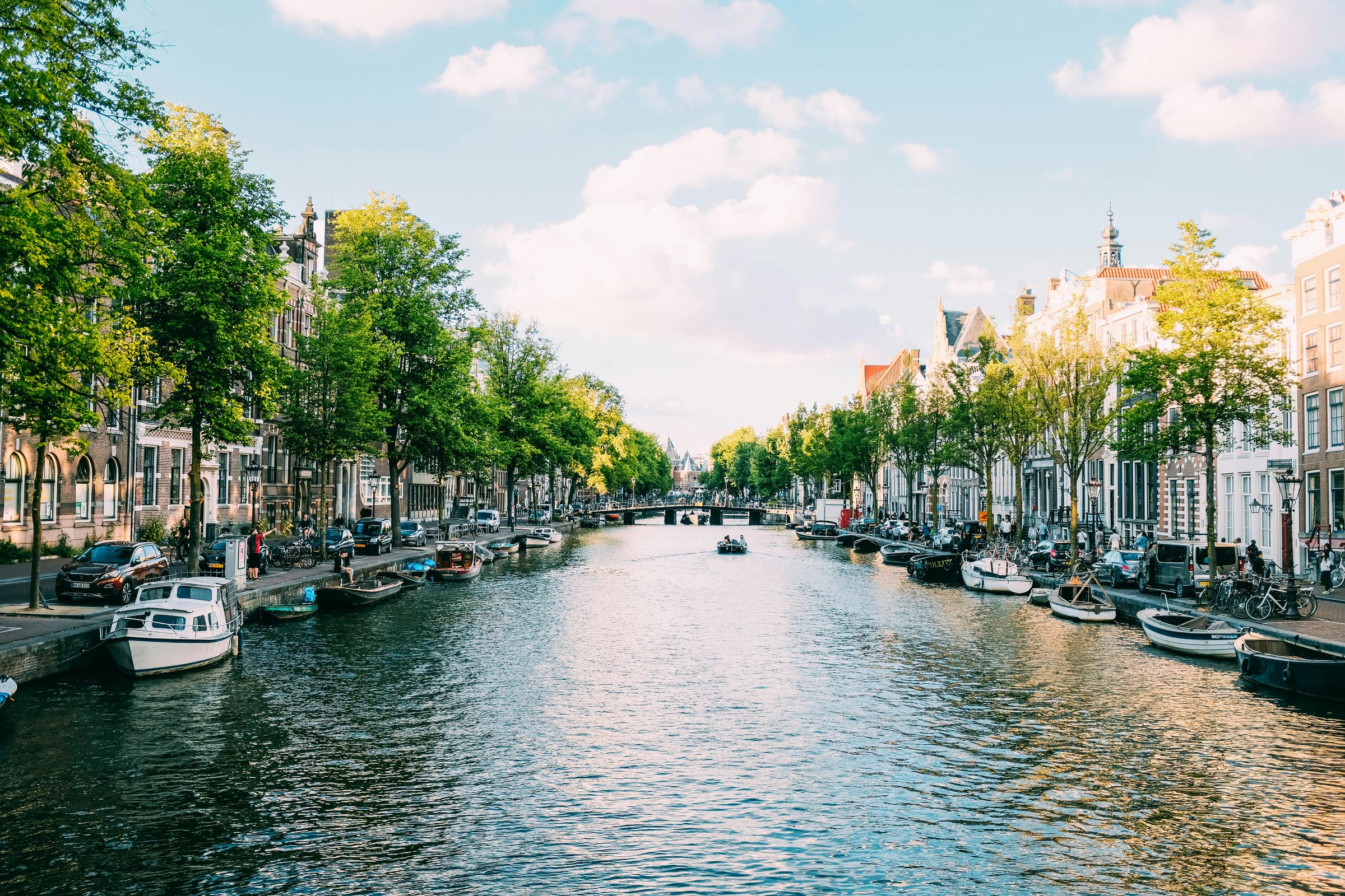 Kanal Amsterdam dengan rumah-rumah tua, perahu, dan pepohonan.