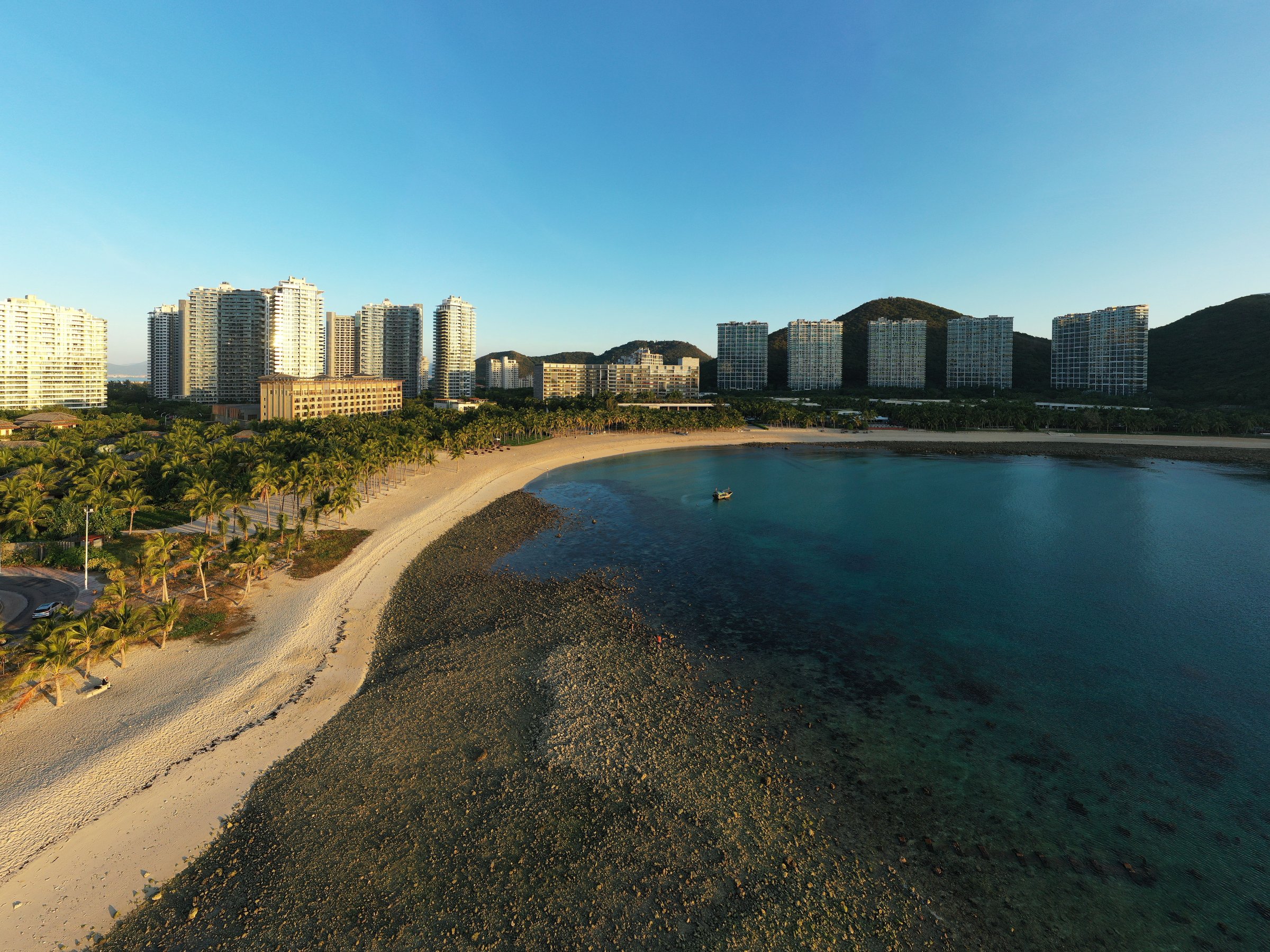 Pemandangan udara pantai Sanya, Hainan, saat senja dengan teluk biru dan bukit hijau