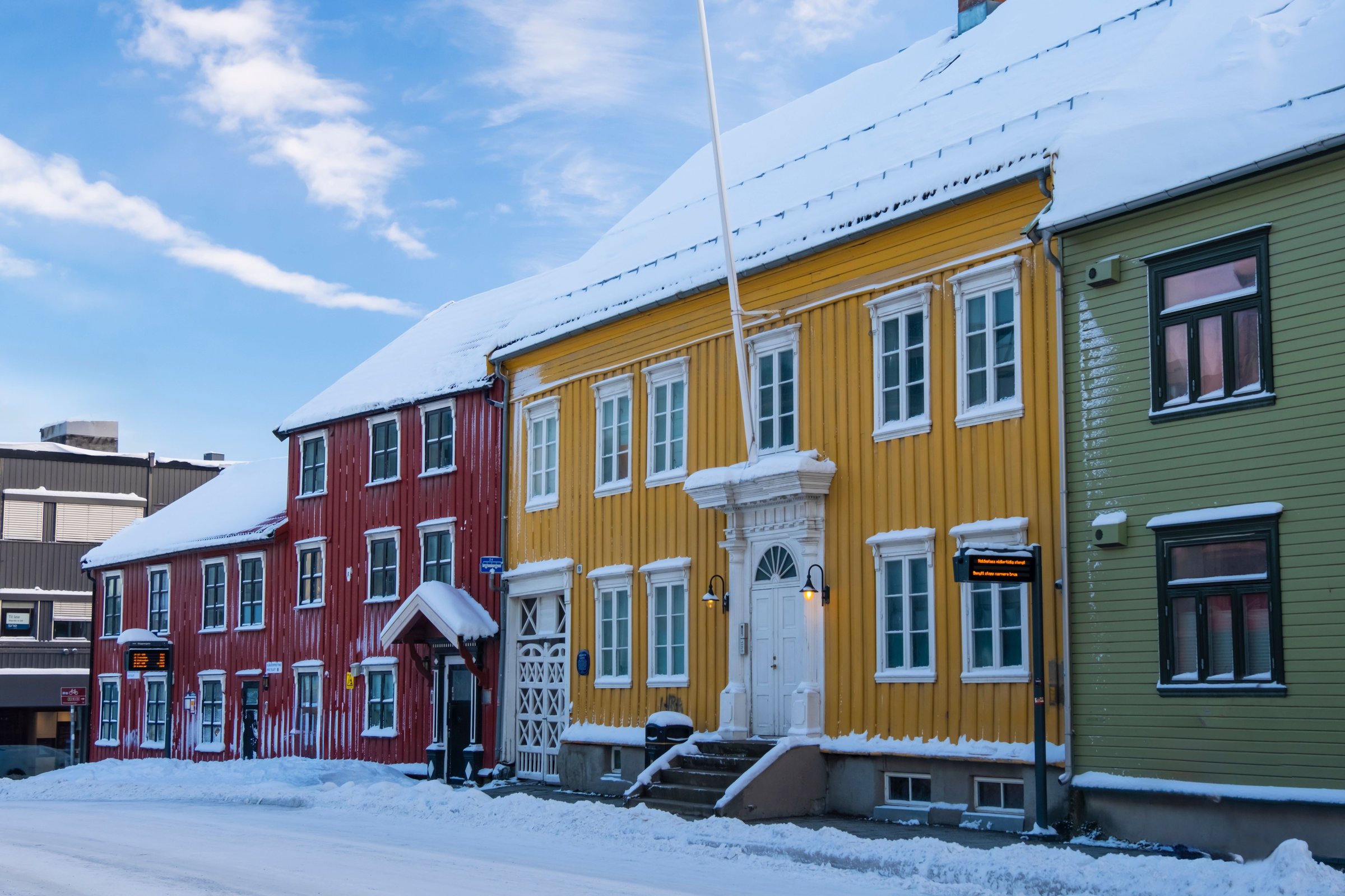 Rumah kayu warna-warni khas Arktik di Tromso dengan atap bersalju dan langit biru