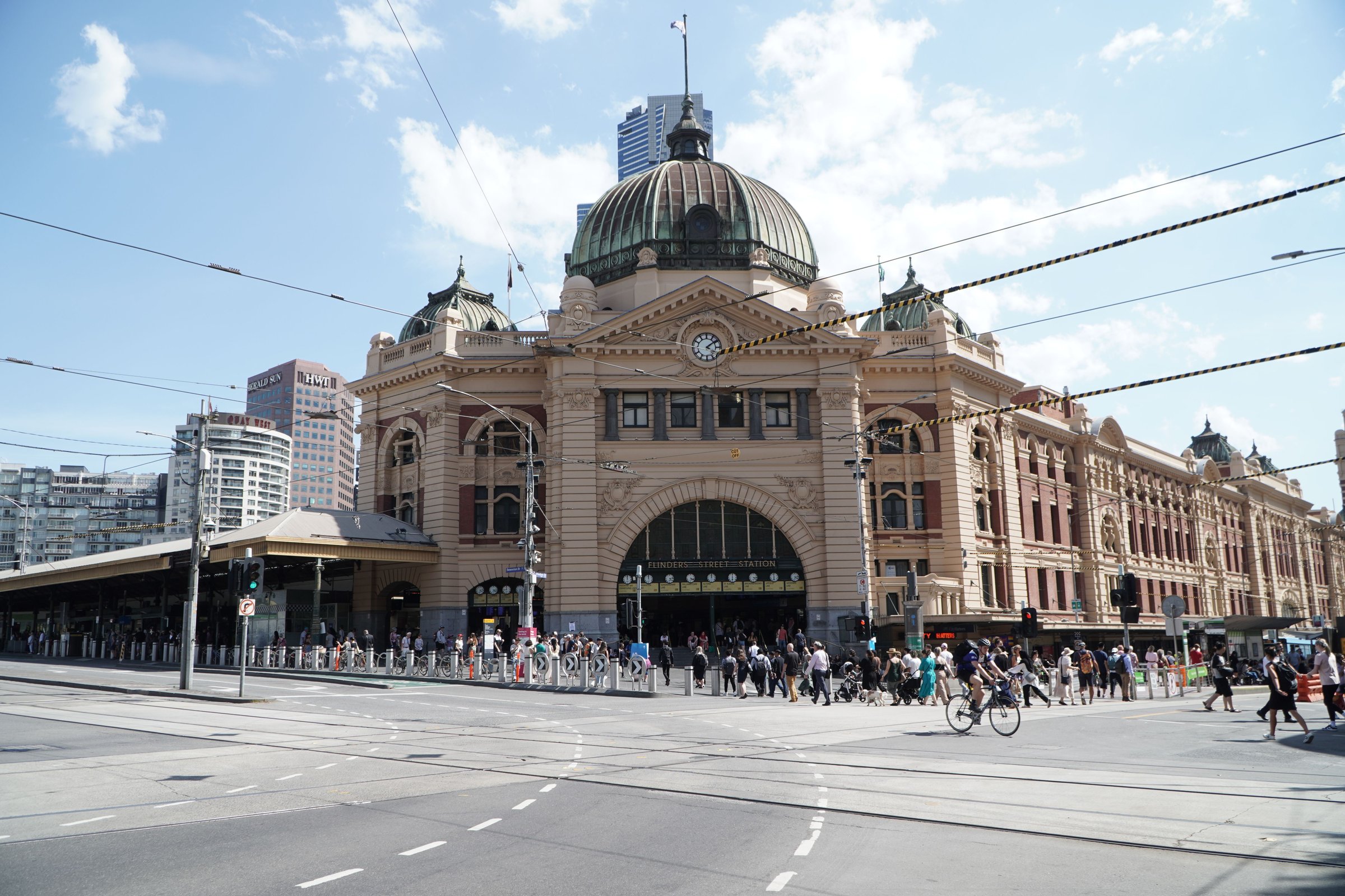 Fasad ikonik Flinders Street Station dengan kubah hijau dan jam besar di bawah langit biru Melbourne