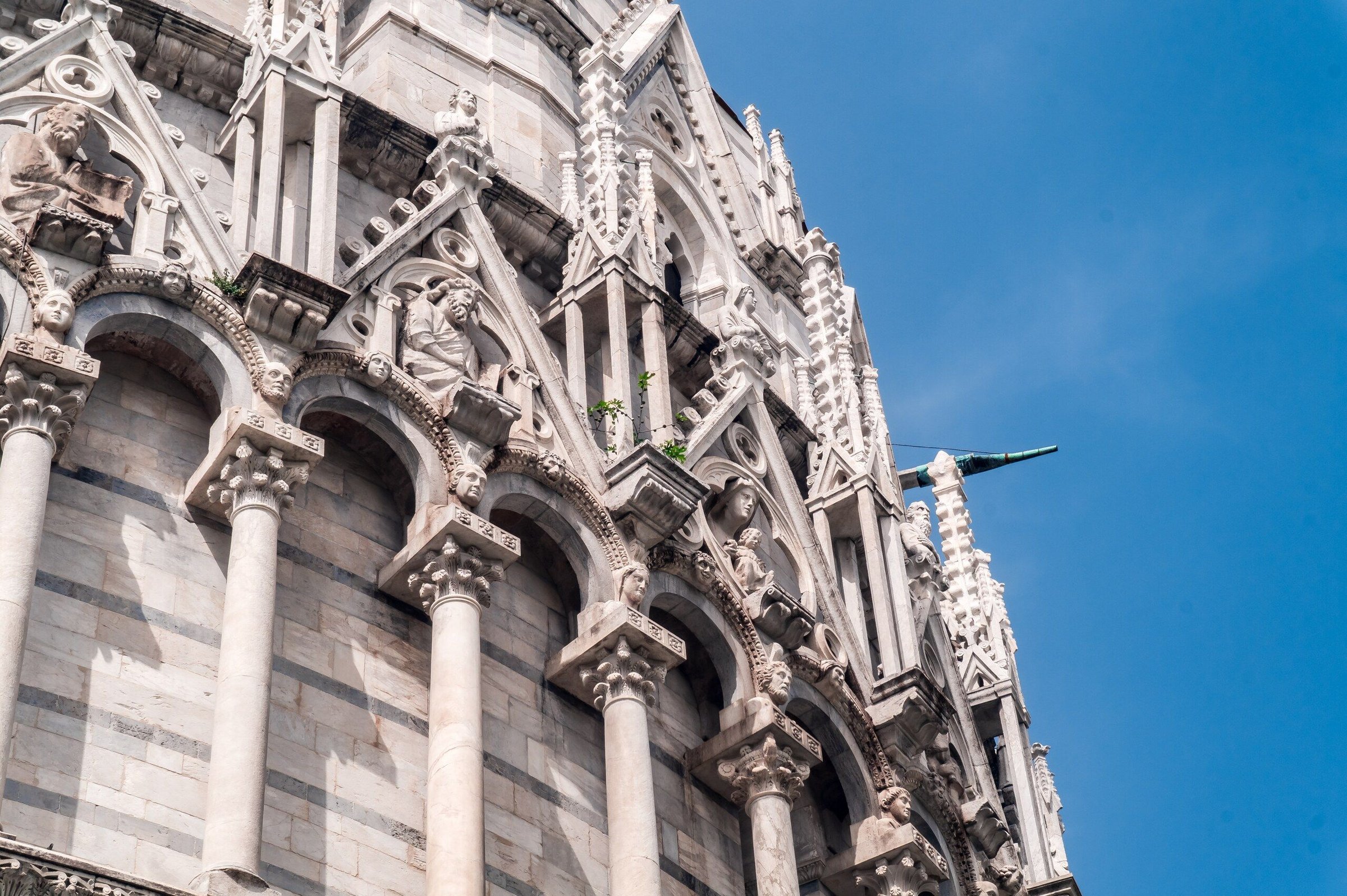 Kubah Baptistery San Giovanni di Pisa dengan Duomo dan menara miring di kejauhan, langit biru.