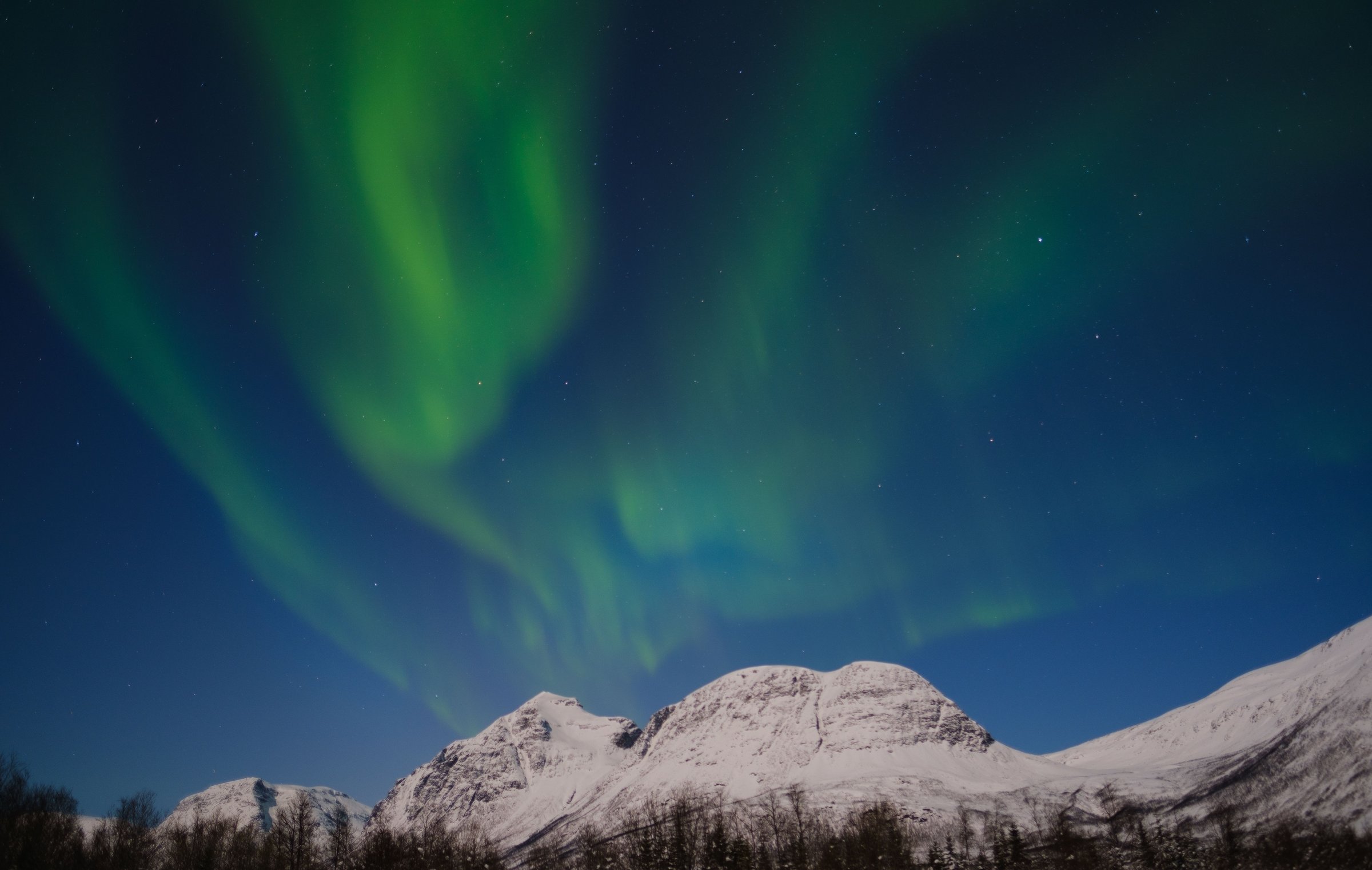 Cahaya aurora borealis hijau menari di atas pegunungan bersalju dengan langit malam berbintang