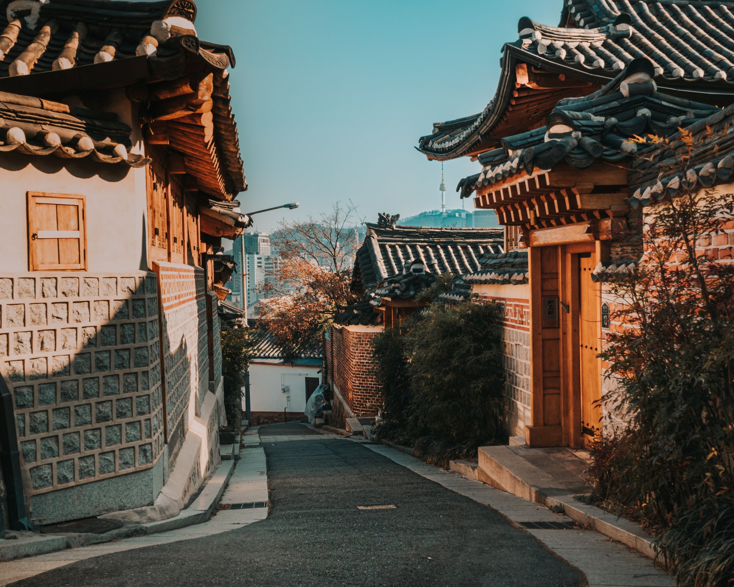 Gang hanok tradisional Bukchon dengan atap genteng melengkung diterangi cahaya sore