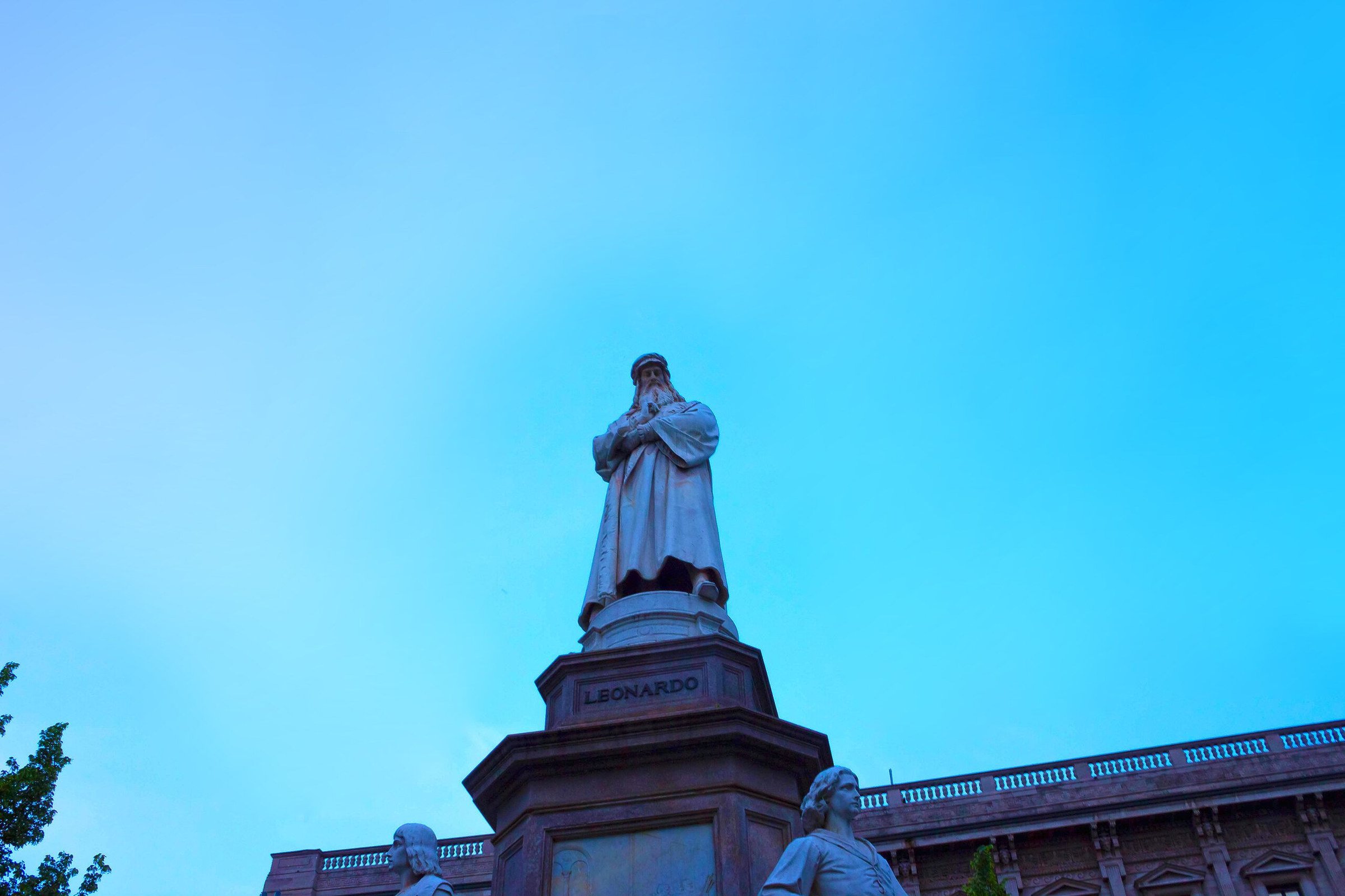 Patung Leonardo da Vinci di Piazza della Scala, Milan, dilihat dari bawah dengan langit biru.