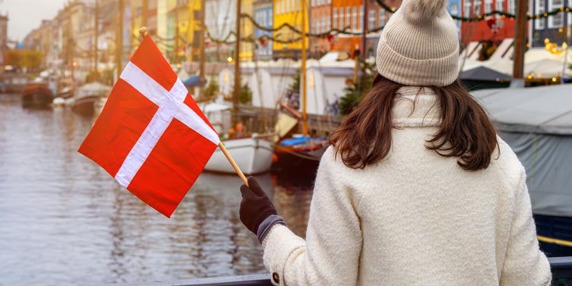 Wisatawan berjaket putih memegang bendera Denmark menghadap kanal Nyhavn Kopenhagen