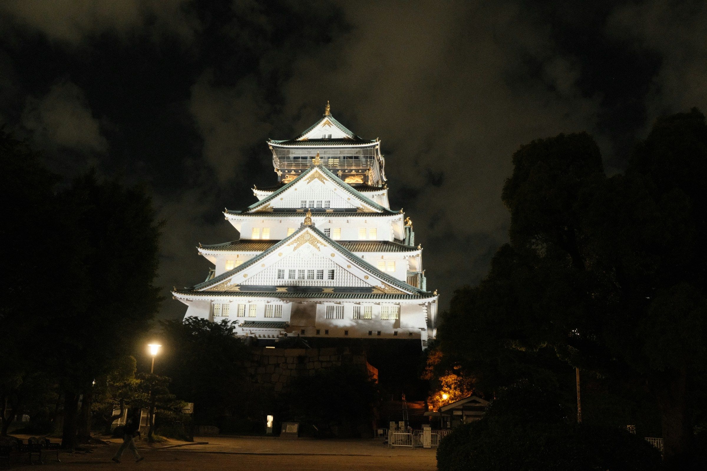 Osaka Castle bercahaya di malam hari di bawah langit gelap dramatis