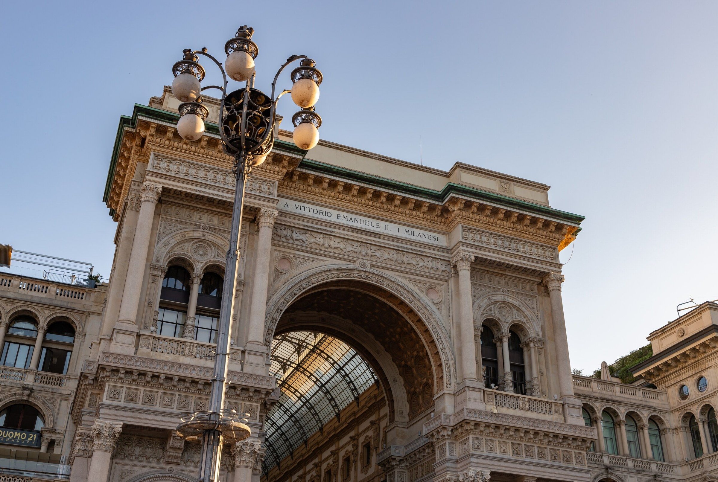 Gerbang lengkung Galleria Vittorio Emanuele II di Milan dari sudut rendah, dengan lampu jalan klasik.