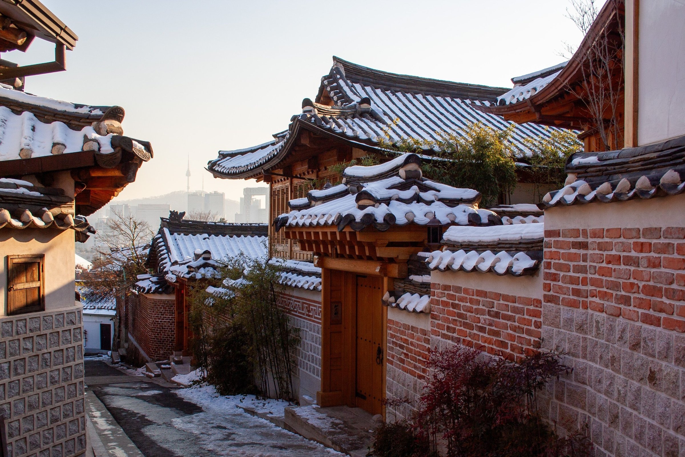 Gang rumah hanok tradisional Seoul dengan atap genteng berselimut salju di hari cerah